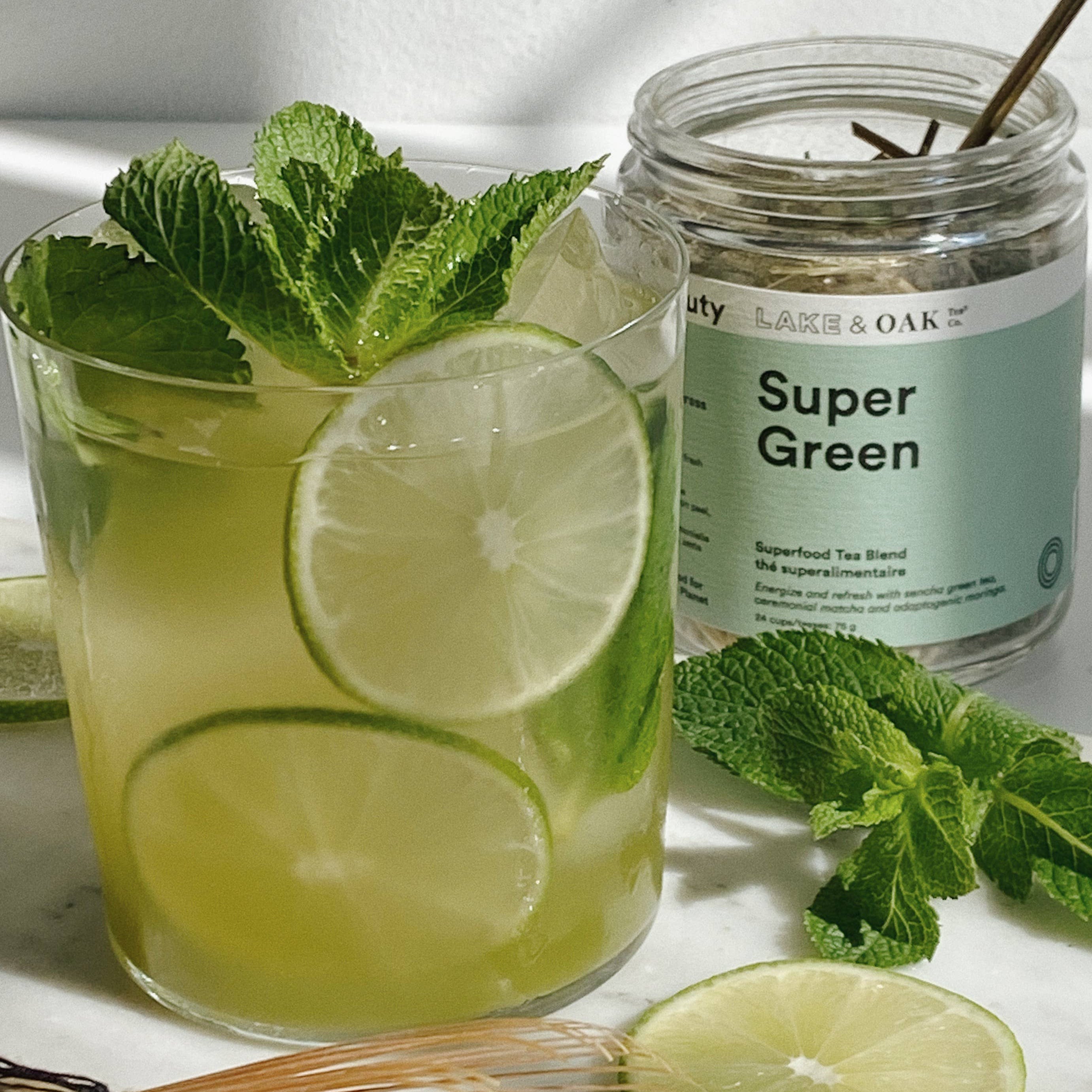 Green drink with lime slices and mint leaves next to a jar labeled &