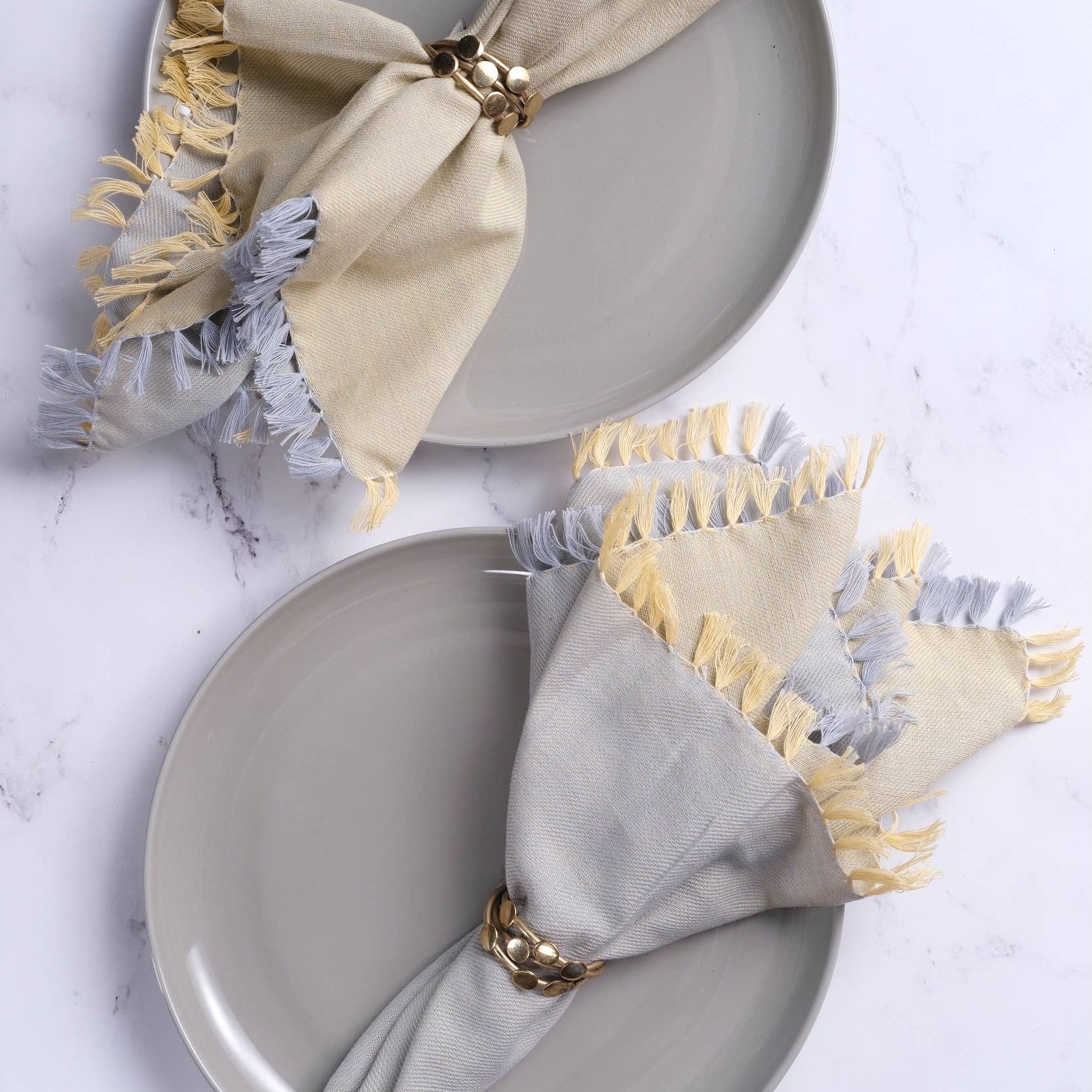 Gray plates with folded napkins featuring fringe details on a light gray background
