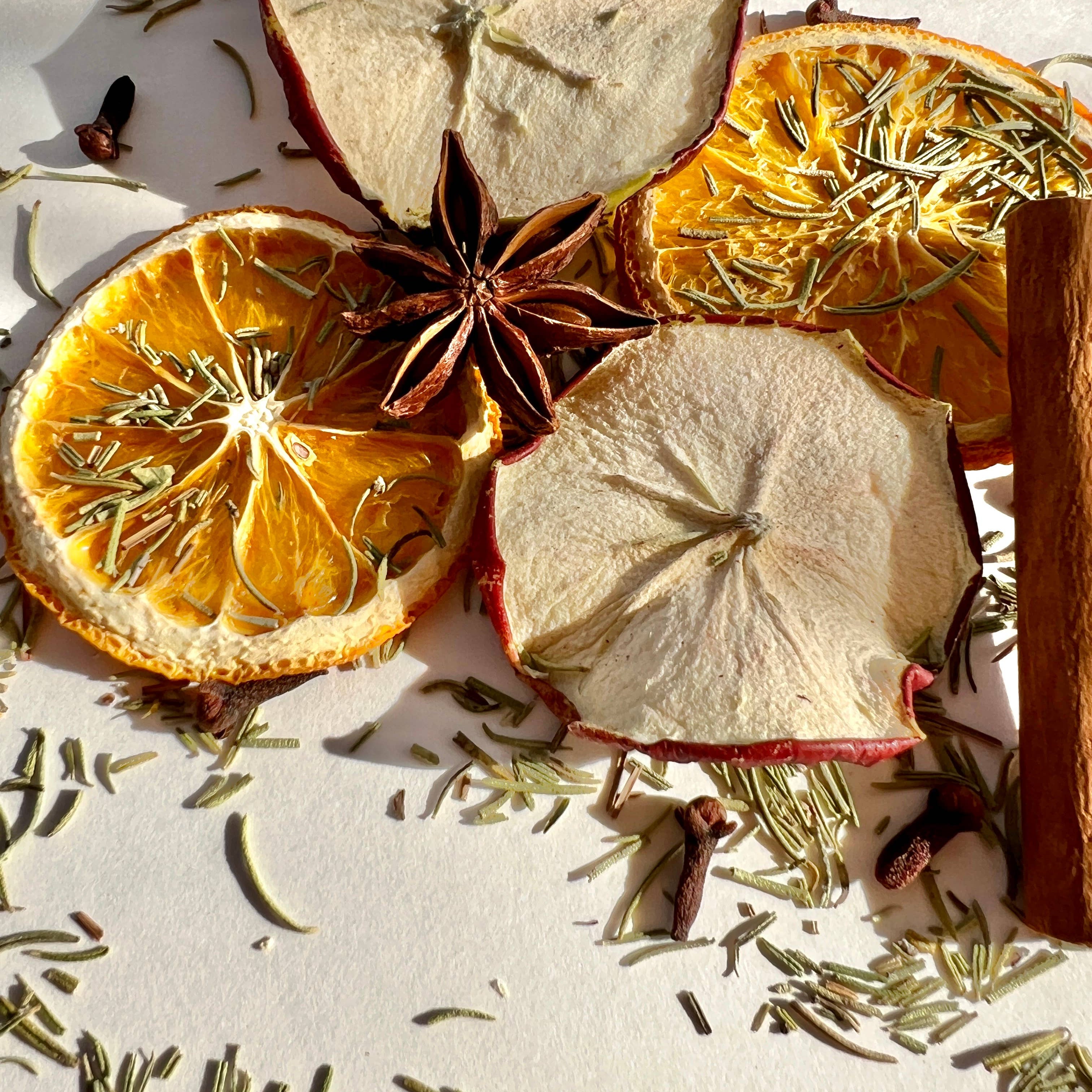 Dried fruits and herbs including apples, oranges, cinnamon sticks, and rosemary on a light background