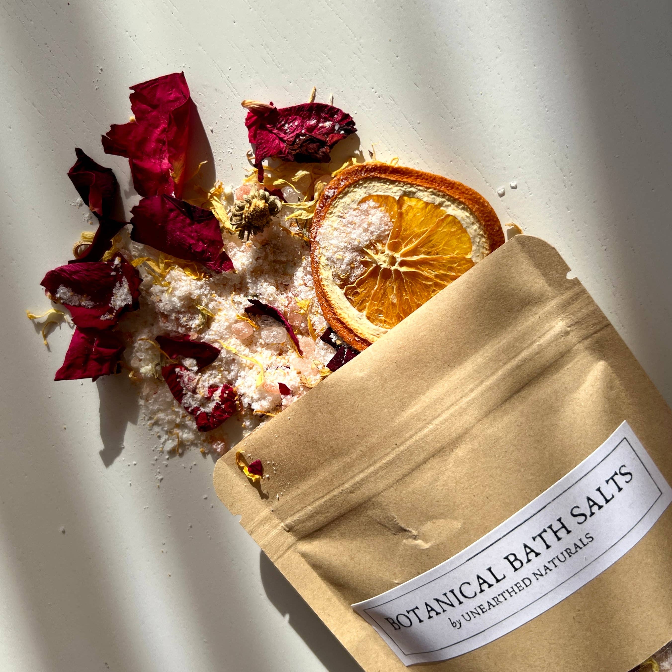 Bag of botanical bath salts with dried flowers and orange slices on a light background