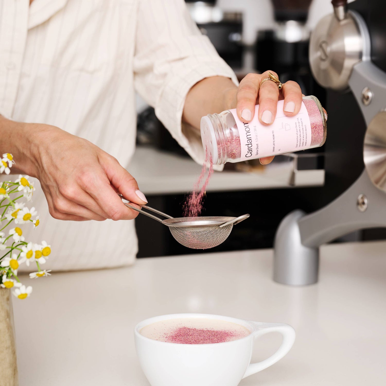 Person adding a pink powder from a canister into a white mug on a kitchen counter.