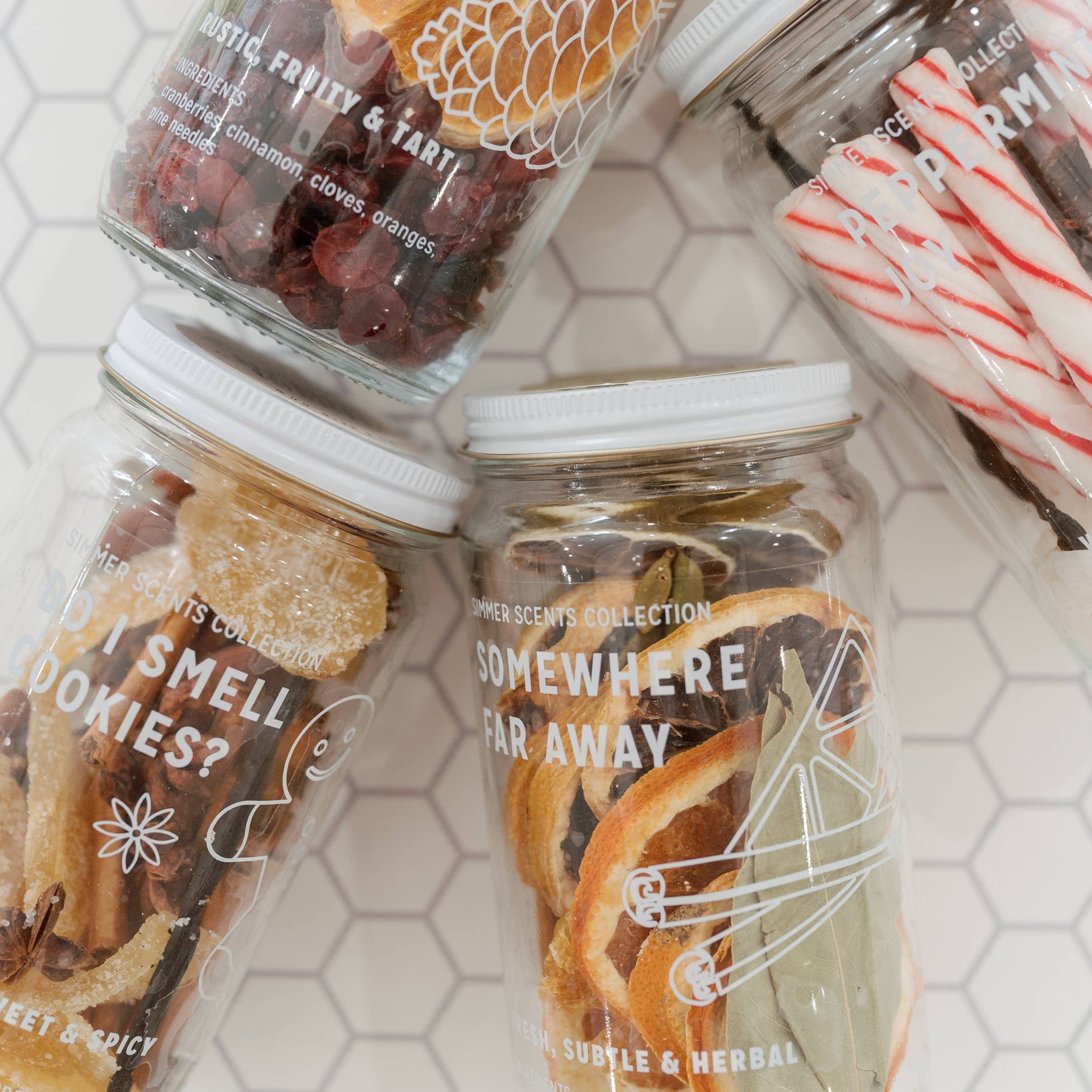 Four glass jars with decorative labels on a hexagonal tile background