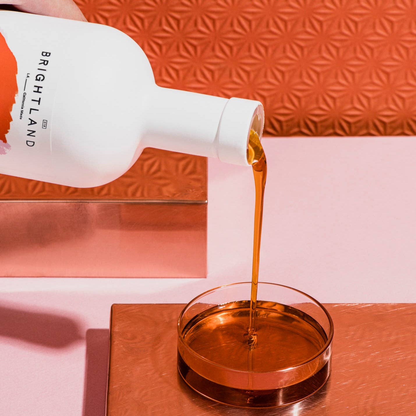 Bottle of Brightland oil being poured into a glass bowl against an orange textured background