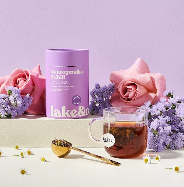 Tea packaging with a glass mug of tea, spoon, and flowers on a light purple background