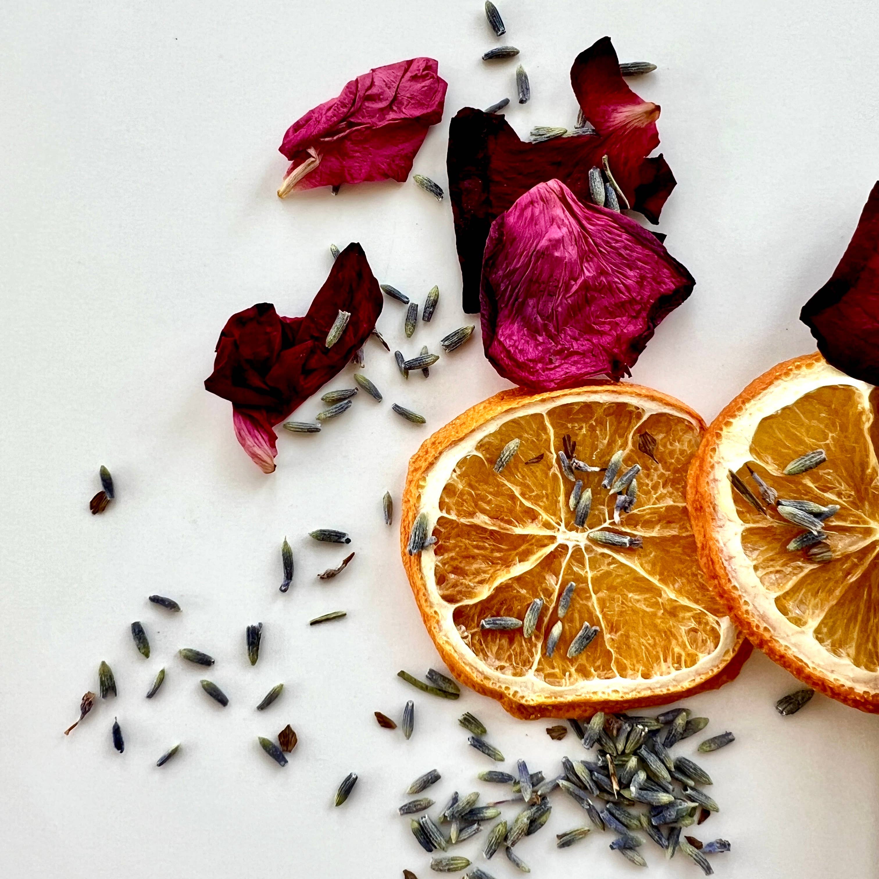 Dried orange slices, lavender flowers, and pink rose petals on a white background