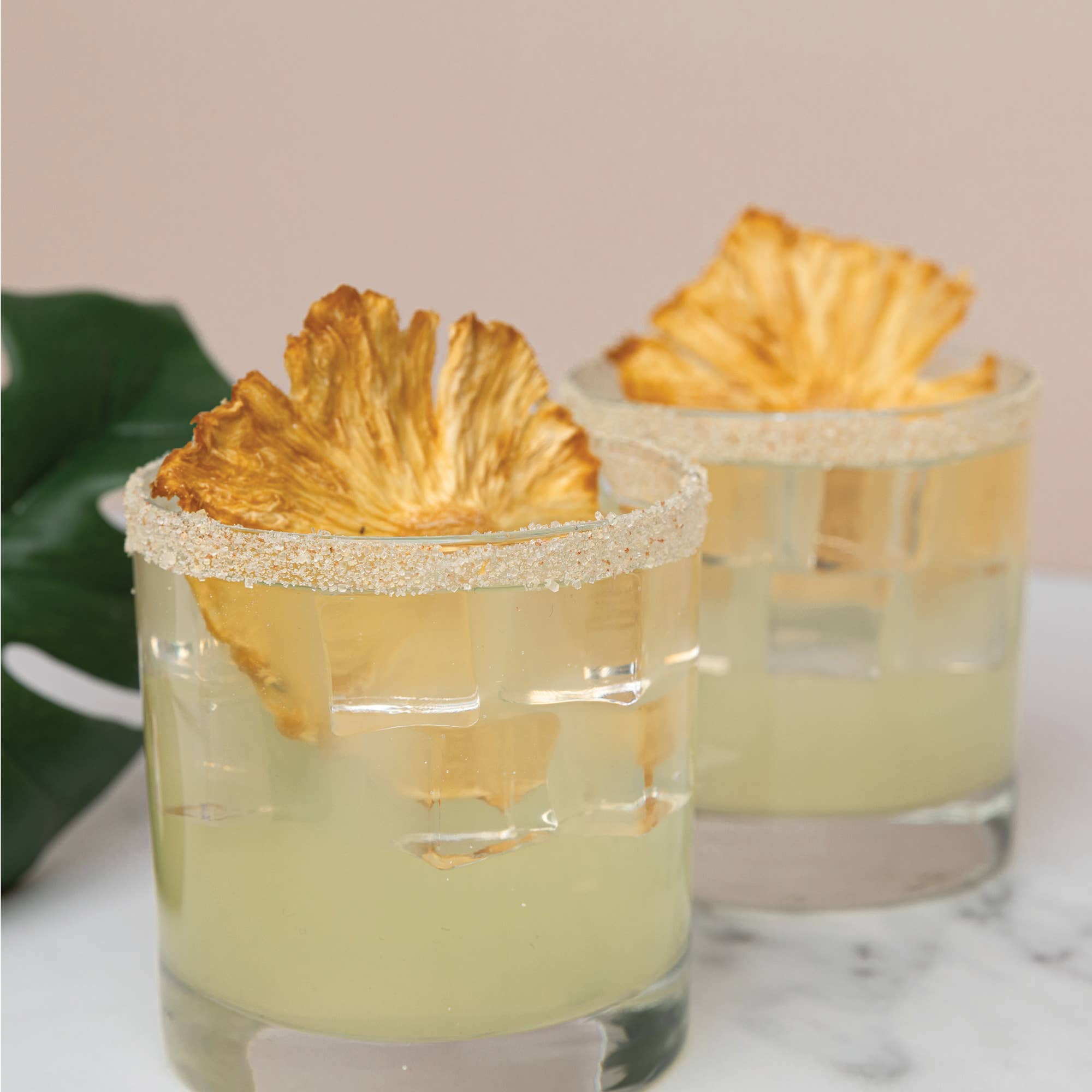 Two cocktails with pineapple slices on a marble surface