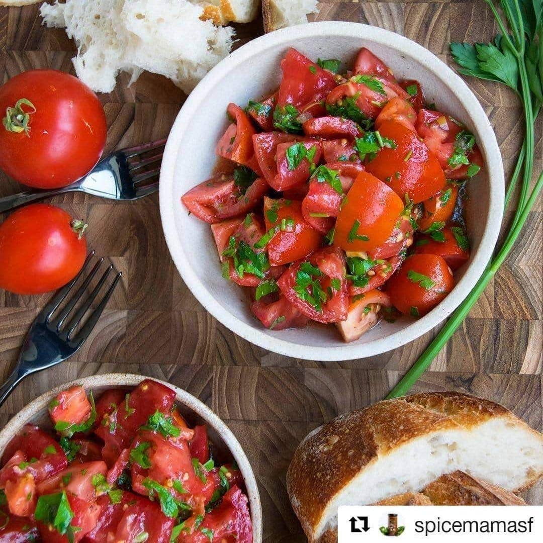 Tomato salad with herbs and sumac in a white bowl on a wooden surface with bread and tomatoes.