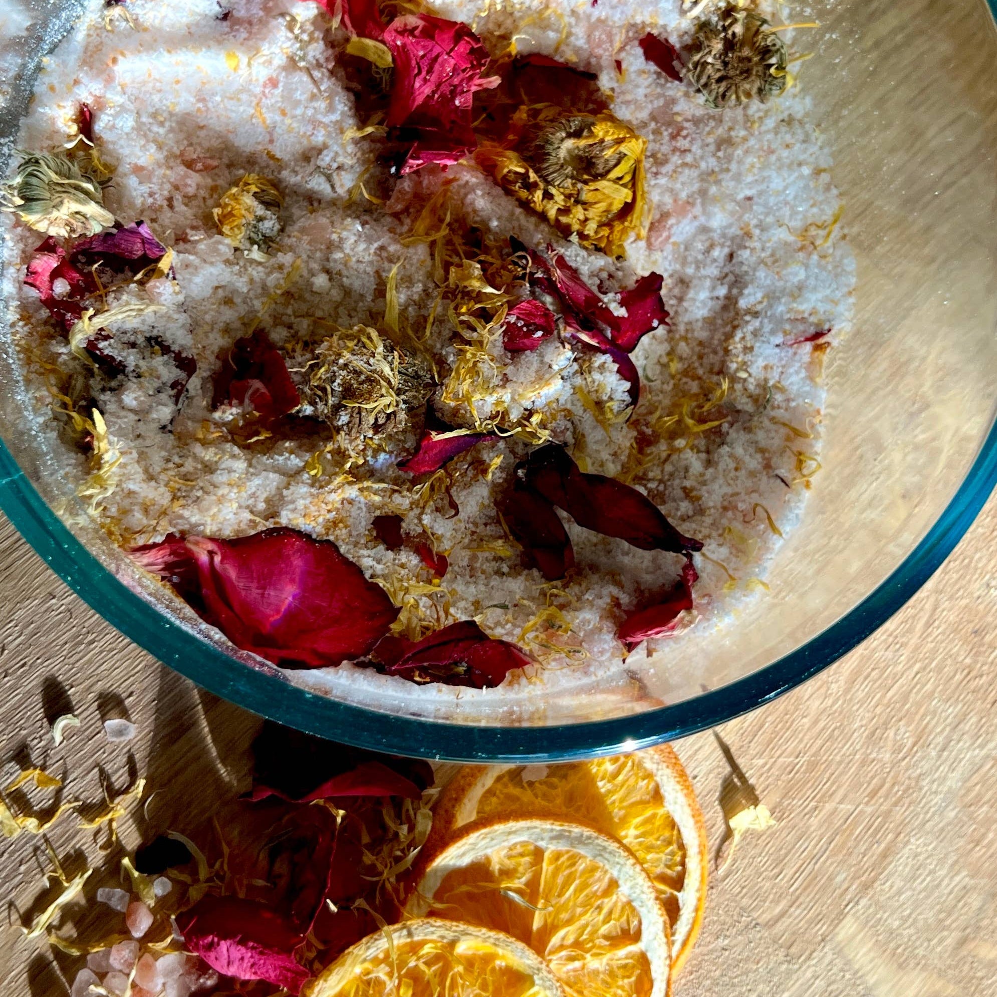 Bowl with bath salts, rose petals, and orange slices on a wooden surface