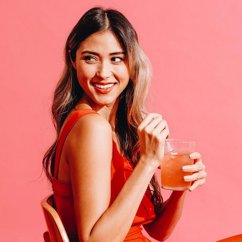 Woman in a red dress holding a glass of pink drink against a pink background