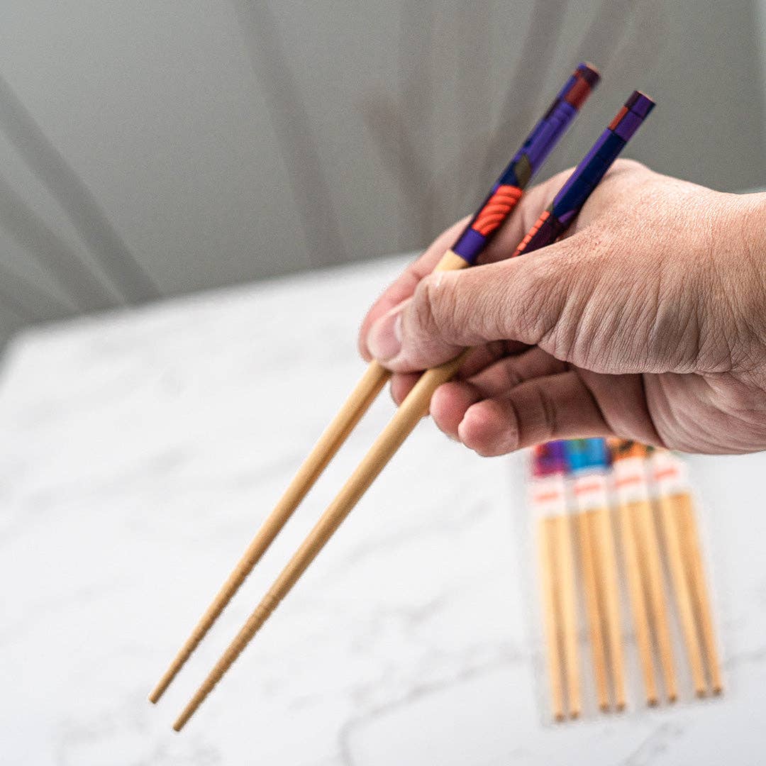 Hand holding a pair of wooden chopsticks with colorful handles on a light background