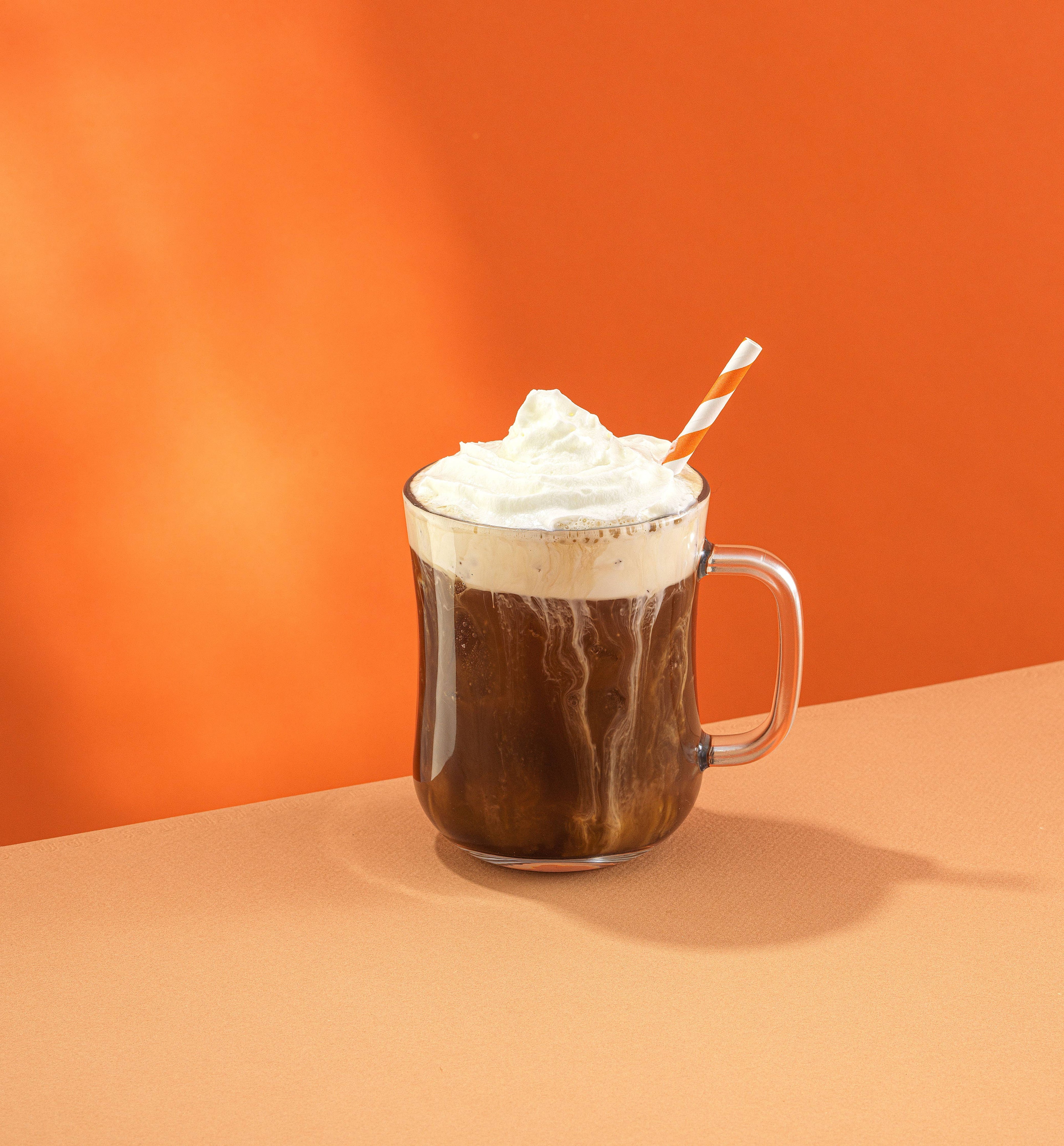 Hot chocolate with whipped cream and a straw on an orange background