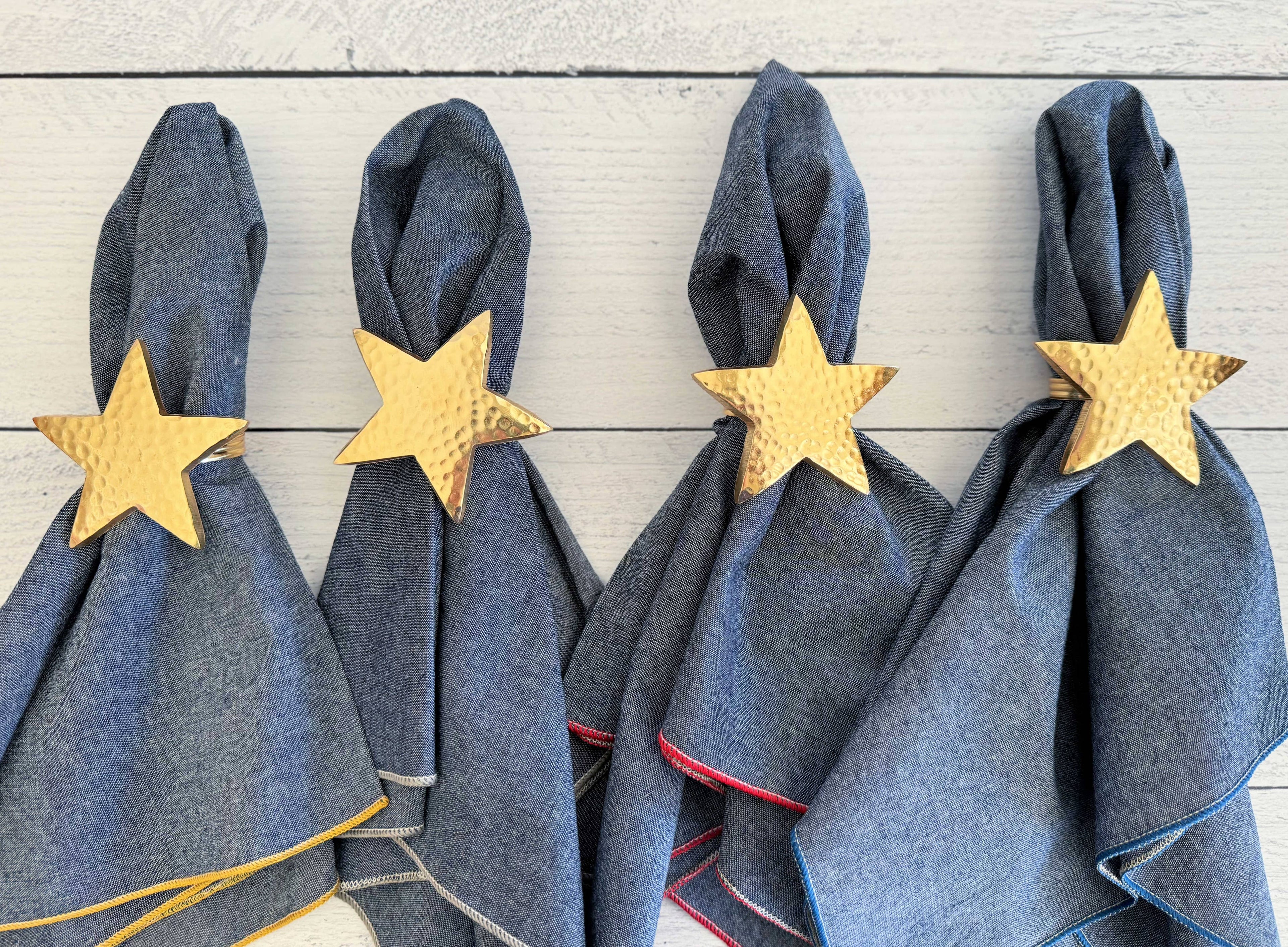 Four denim napkins with gold star napkin rings on a wooden surface