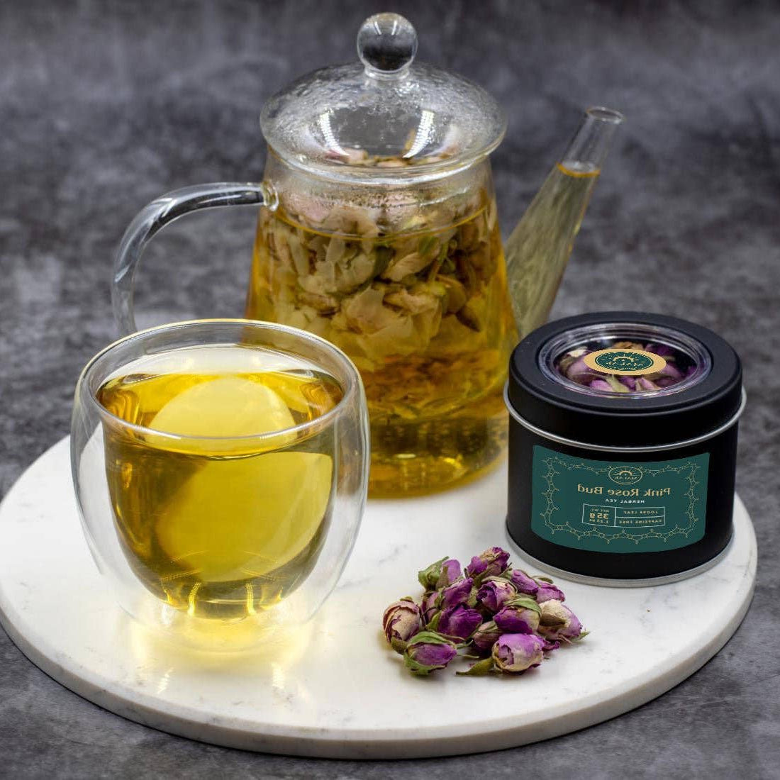 Tea set with a glass teapot, cup, and container on a marble tray with a dark background