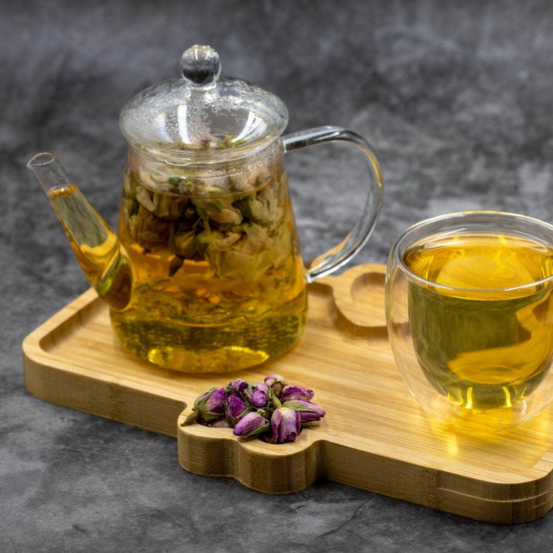 Glass teapot and cup with tea on a wooden tray against a dark background