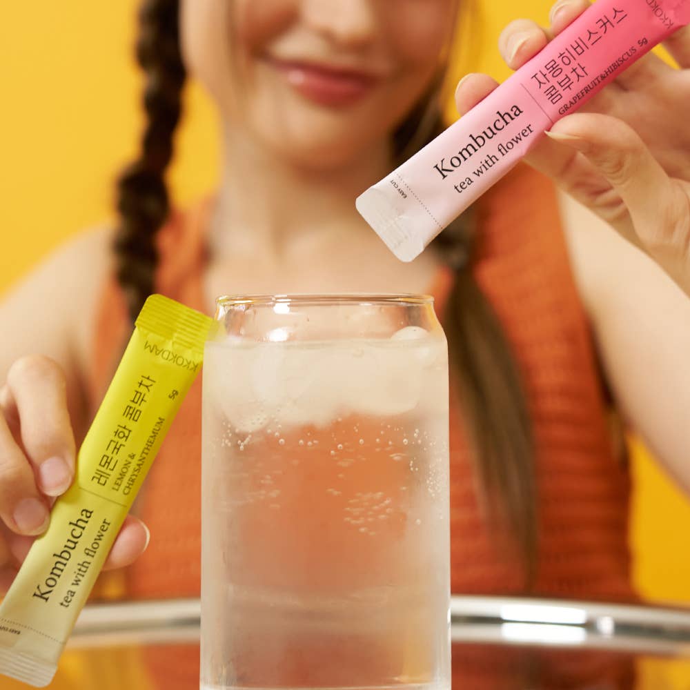 Person holding kombucha tea packets with a glass of ice water on a yellow background