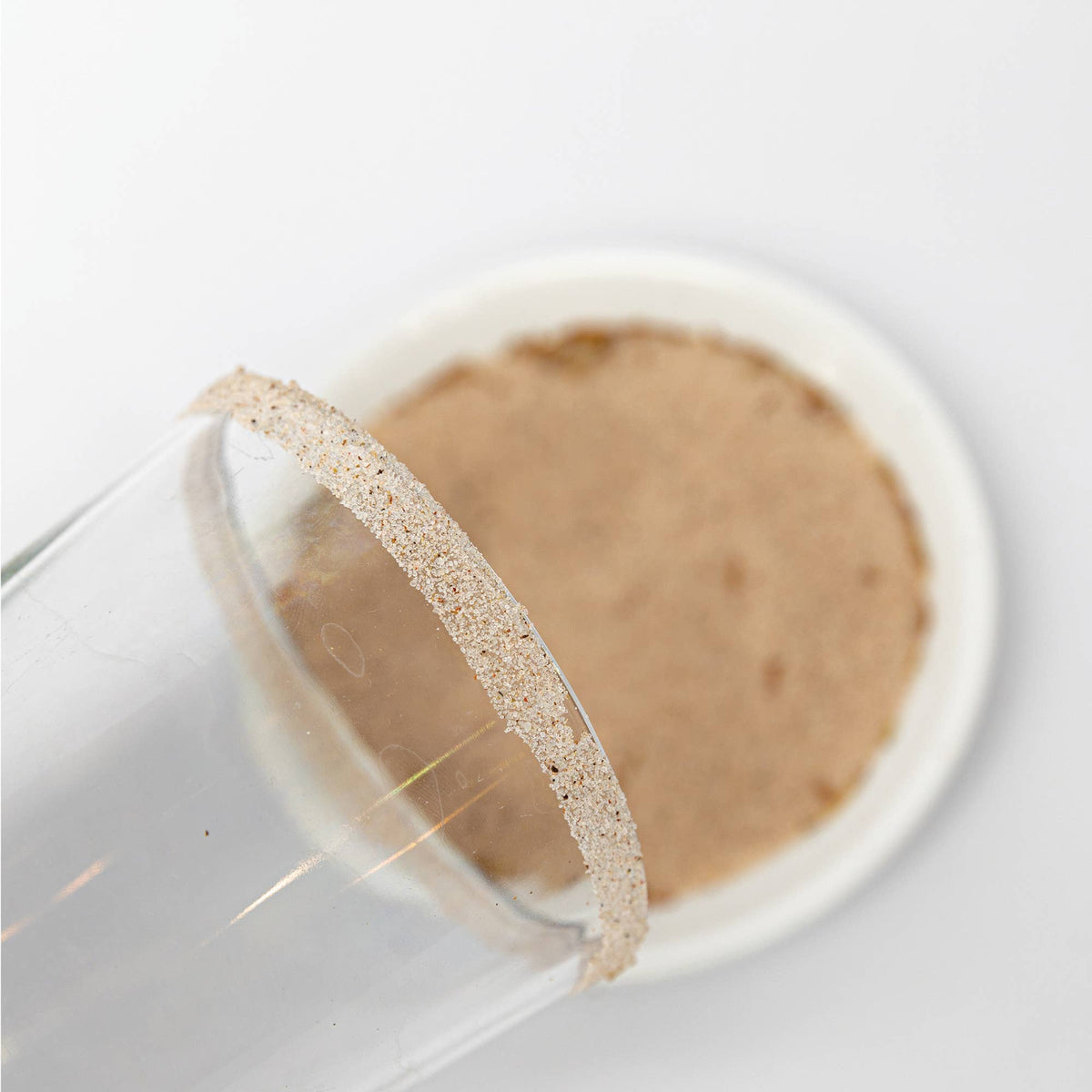Close up of a glass rimmed with bloody mary salt, with a blurred background of a container with the salt.