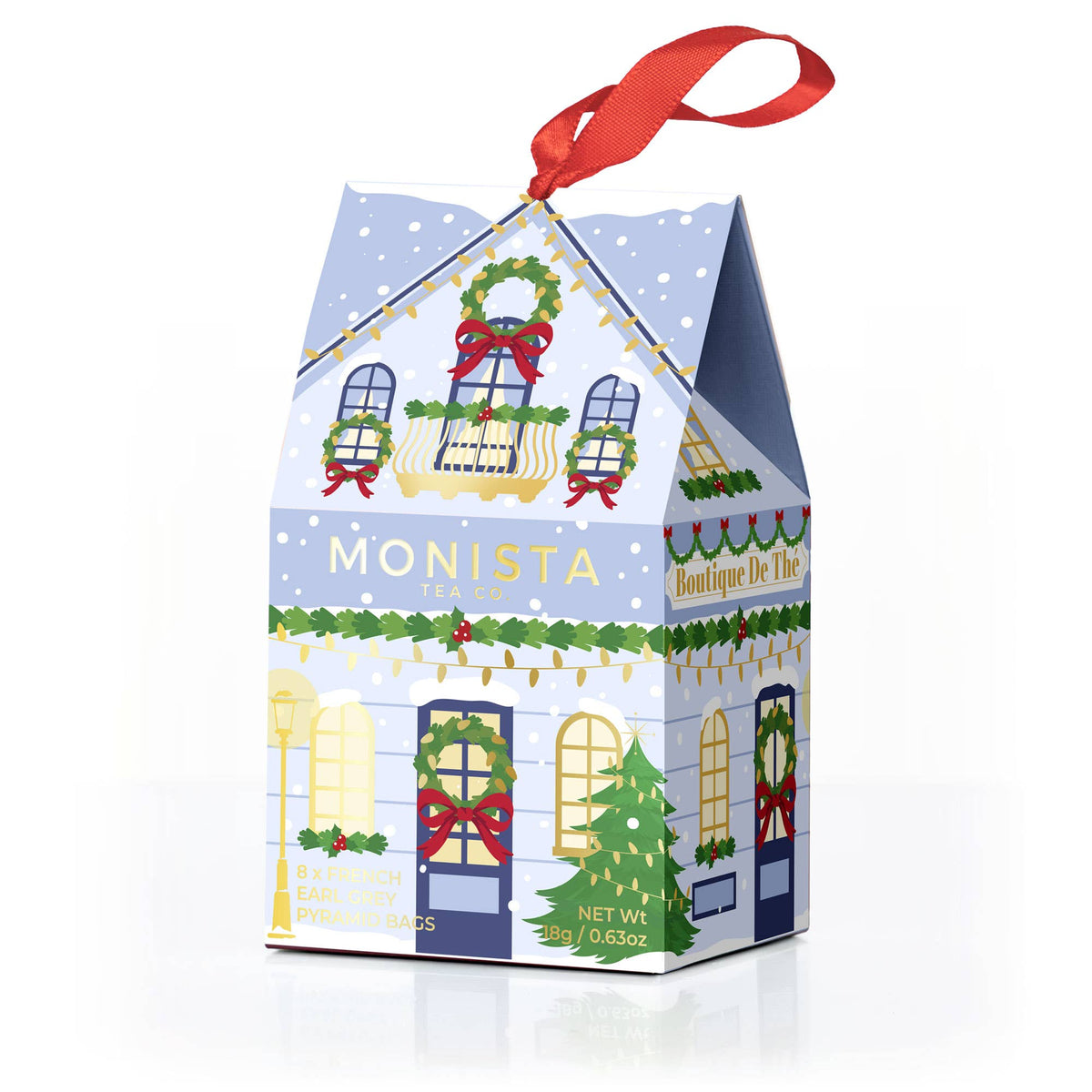 A blue decorative gift box shaped like a house with a red hanging ribbon, printed with a Christmas village scene and the word &