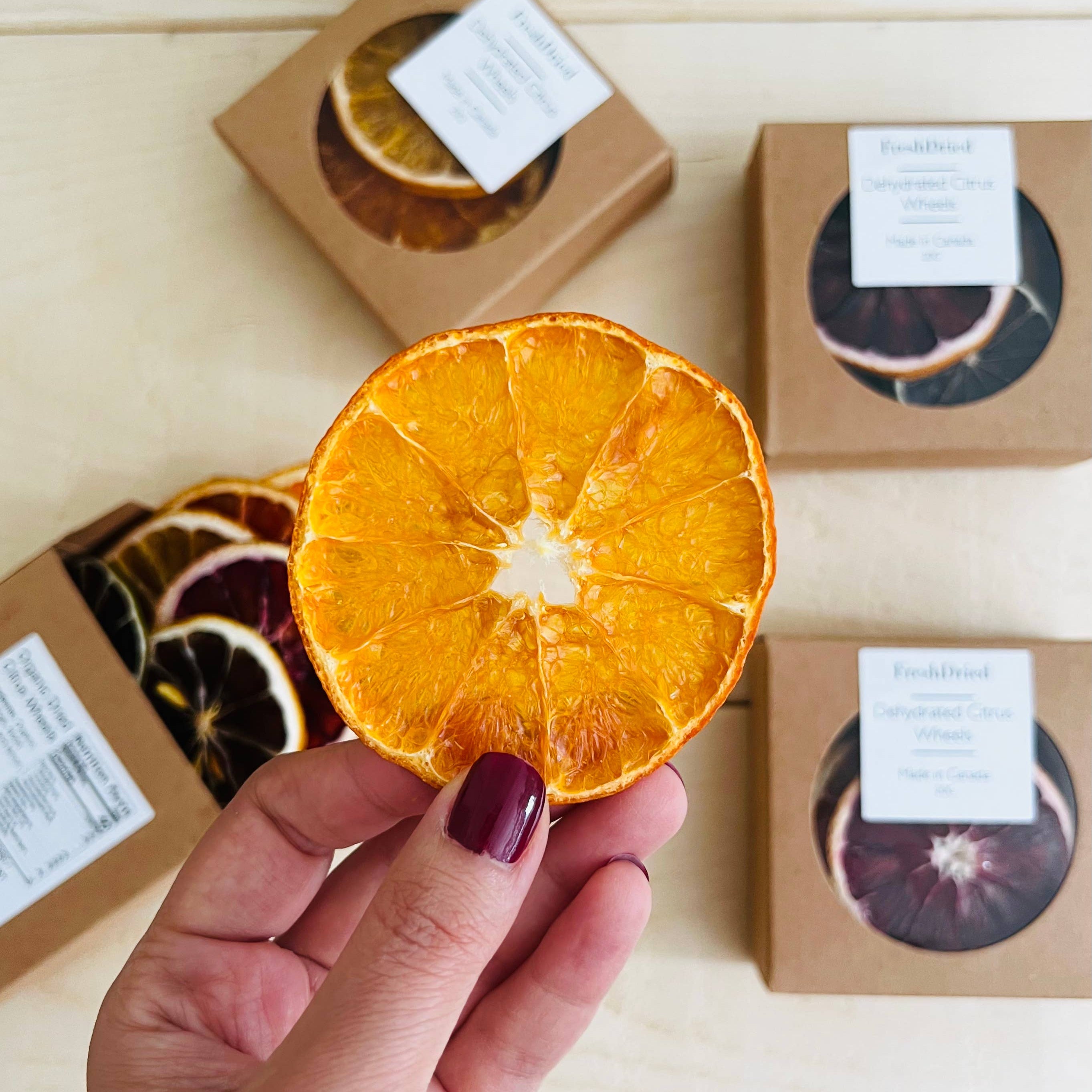 Dried orange slice held by a hand with boxes of dried fruits in the background.
