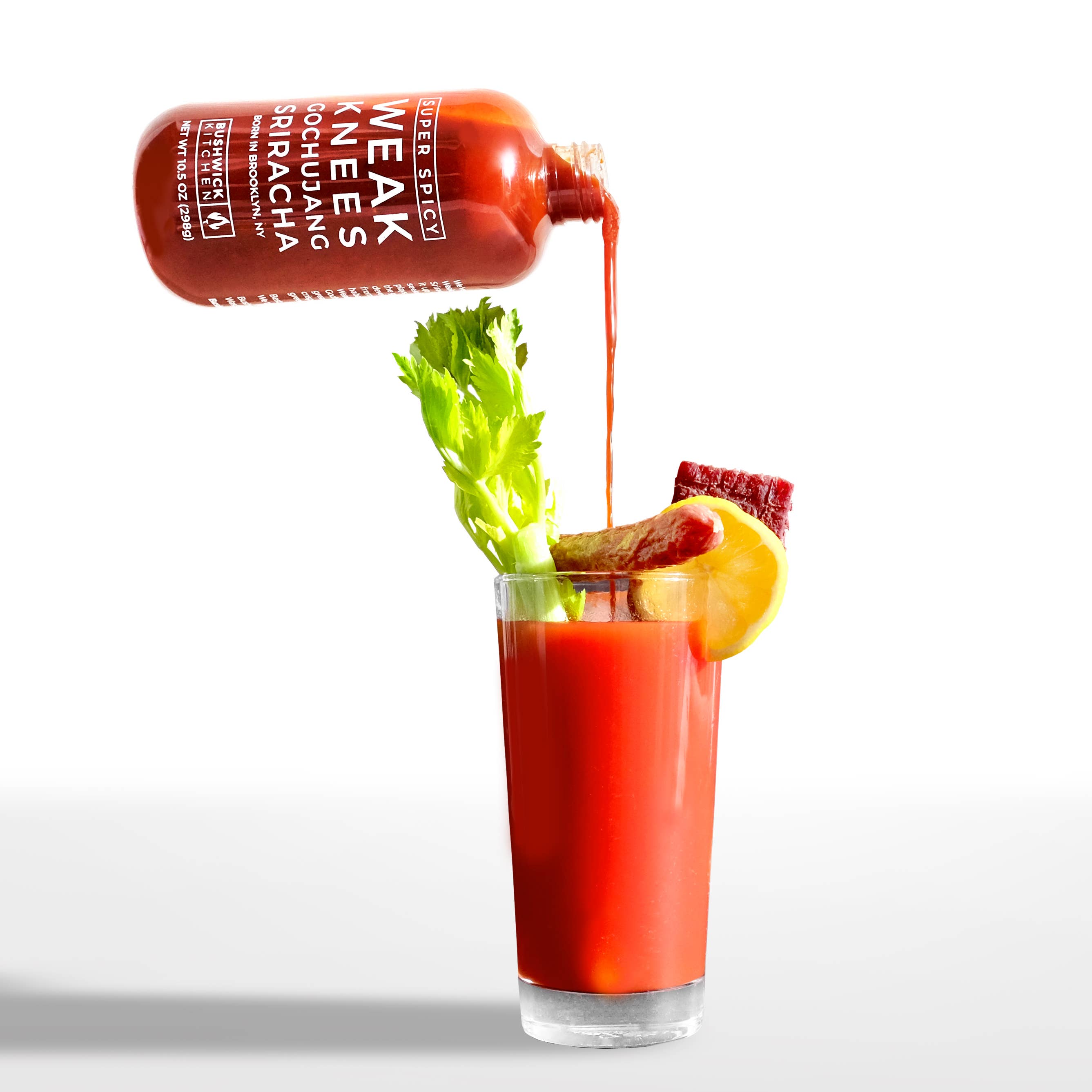 Glass of Bloody Mary with sriracha being poured over it on a white background