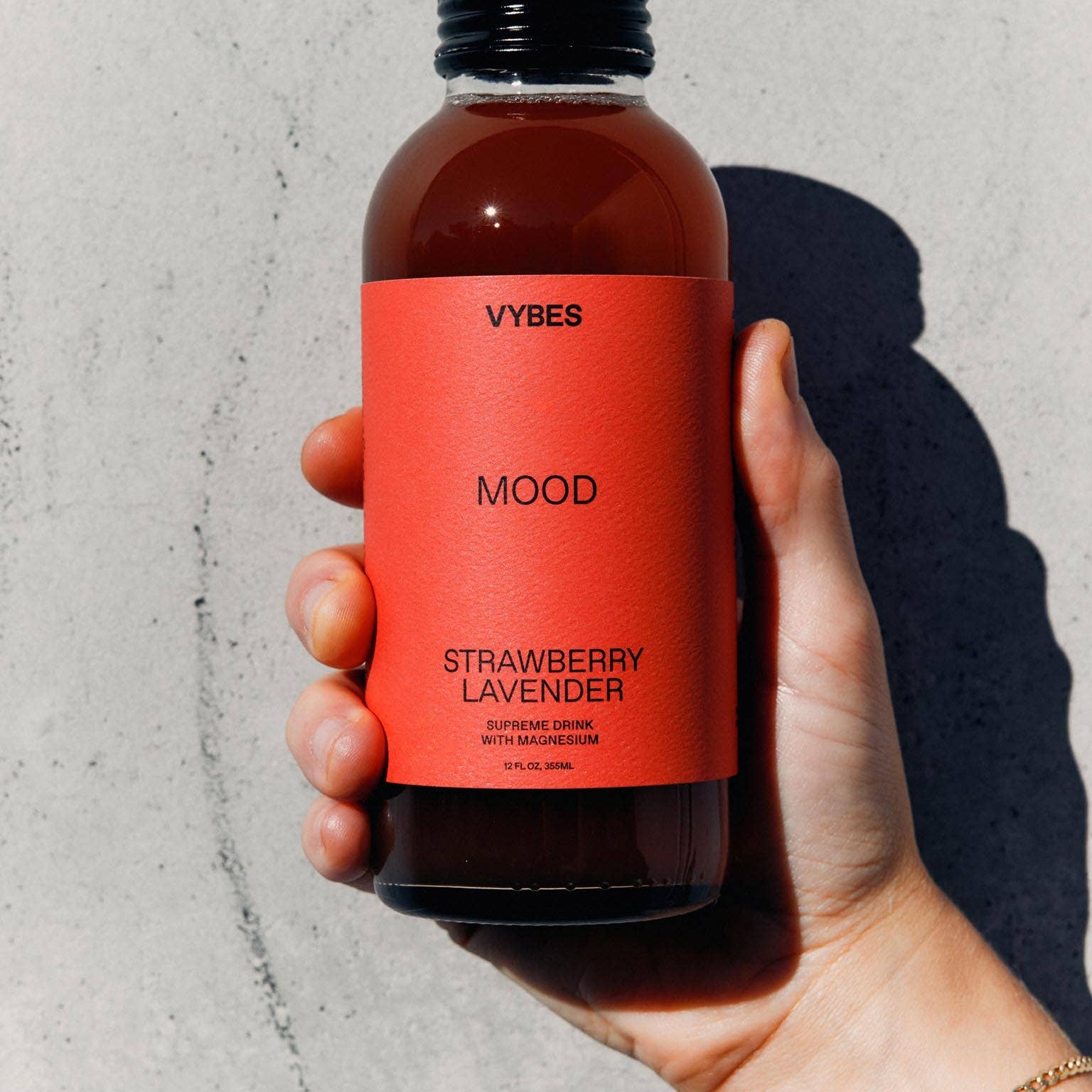 Hand holding a bottle of VYBES Strawberry Lavender Mood supplement against a gray background
