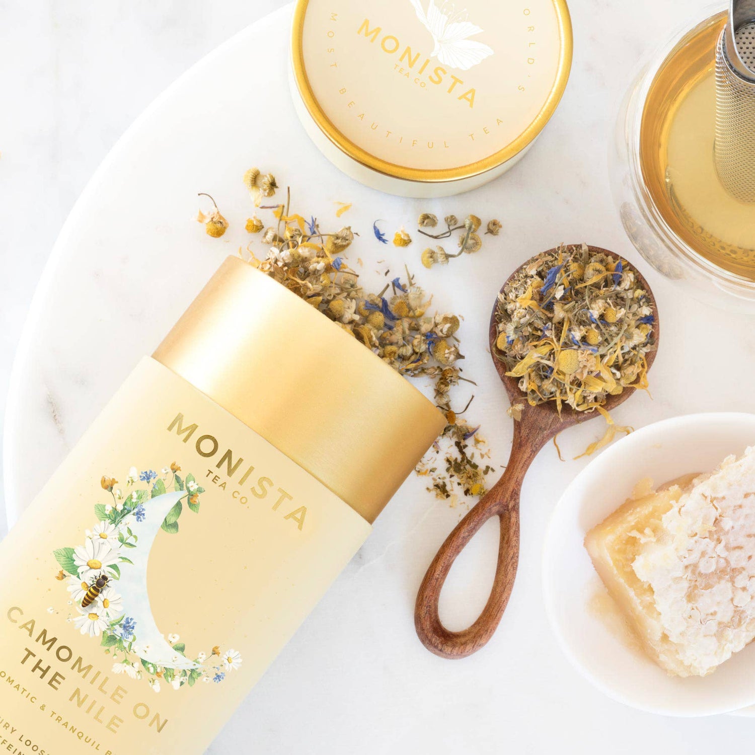 Monista tea packaging with dried herbs and a wooden spoon on a white surface