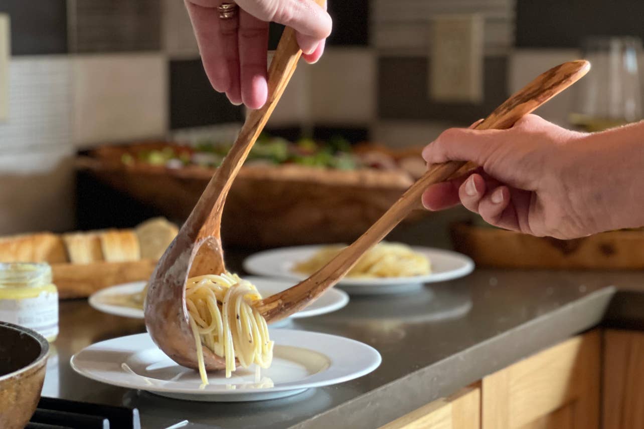 Person serving pasta from an Italian Olivewood Soup and Pasta Ladle