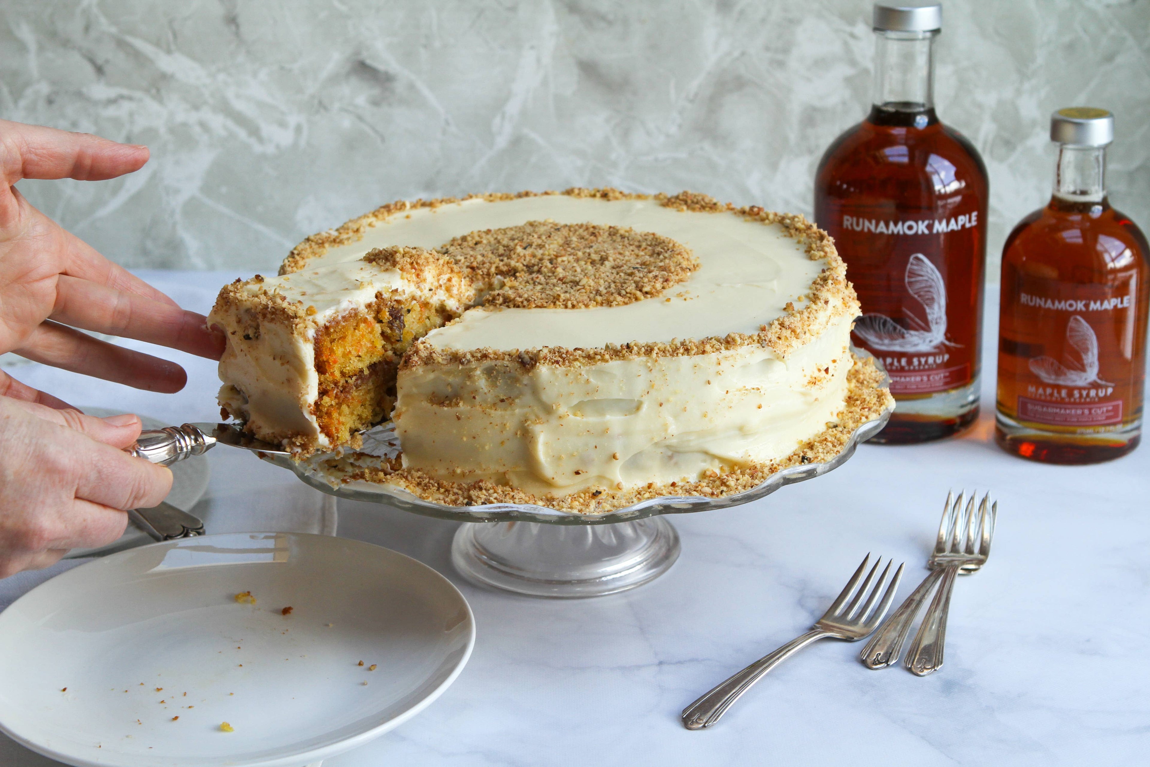 Layered cake with a slice being removed, surrounded by bottles of syrup on a marble surface.