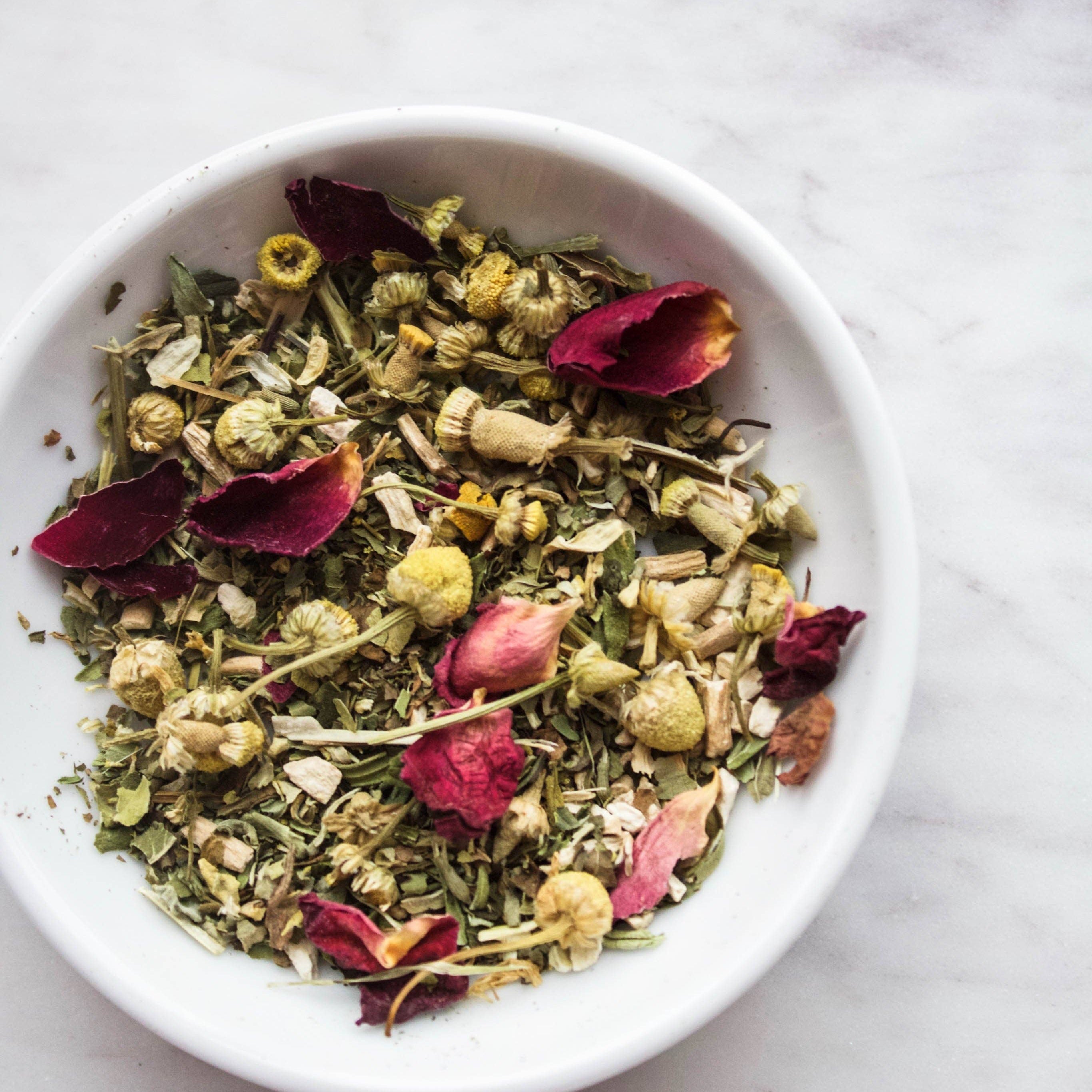 White bowl filled with dried herbs and flowers on a marble surface