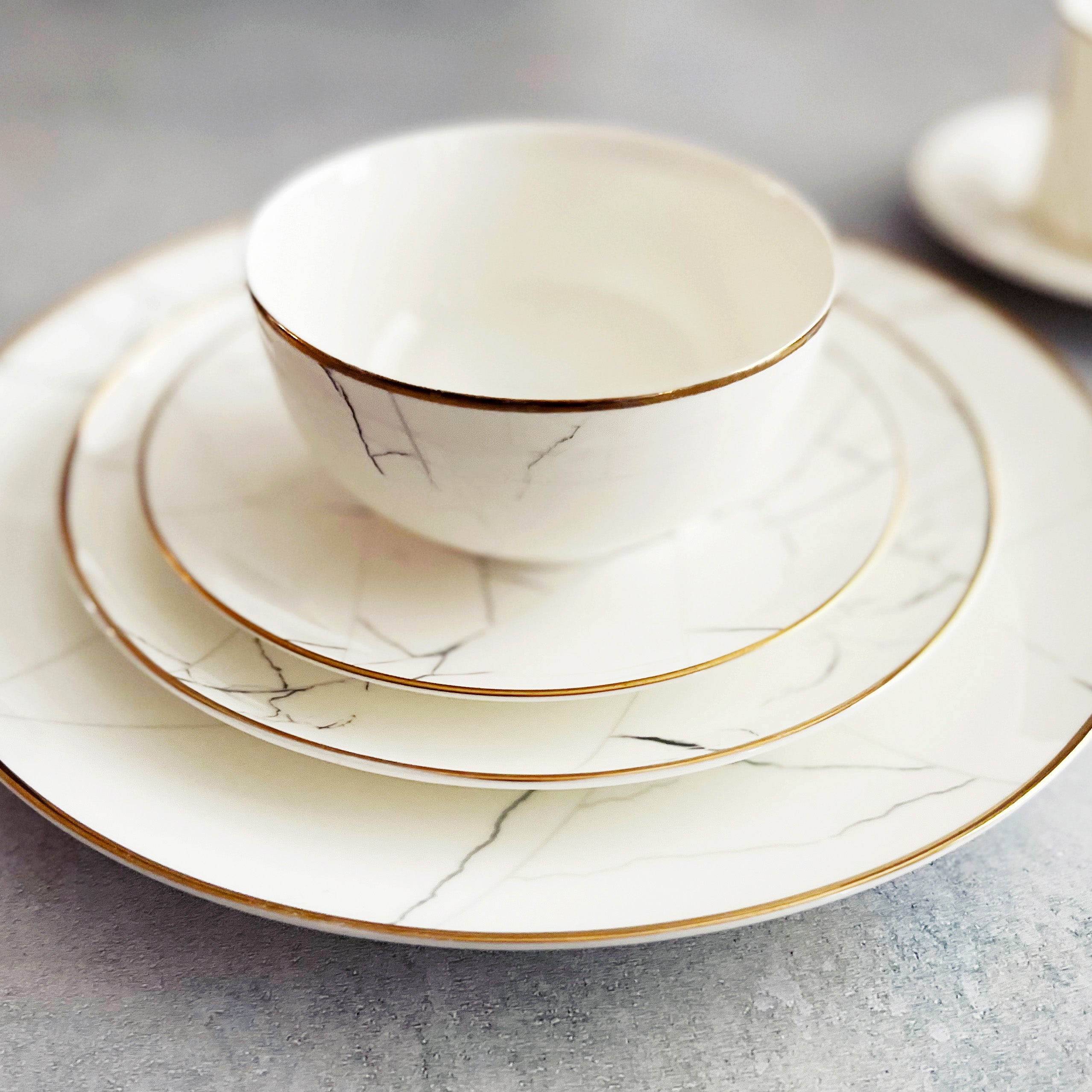Set of ceramic dishes with marble pattern and gold rim on a gray surface