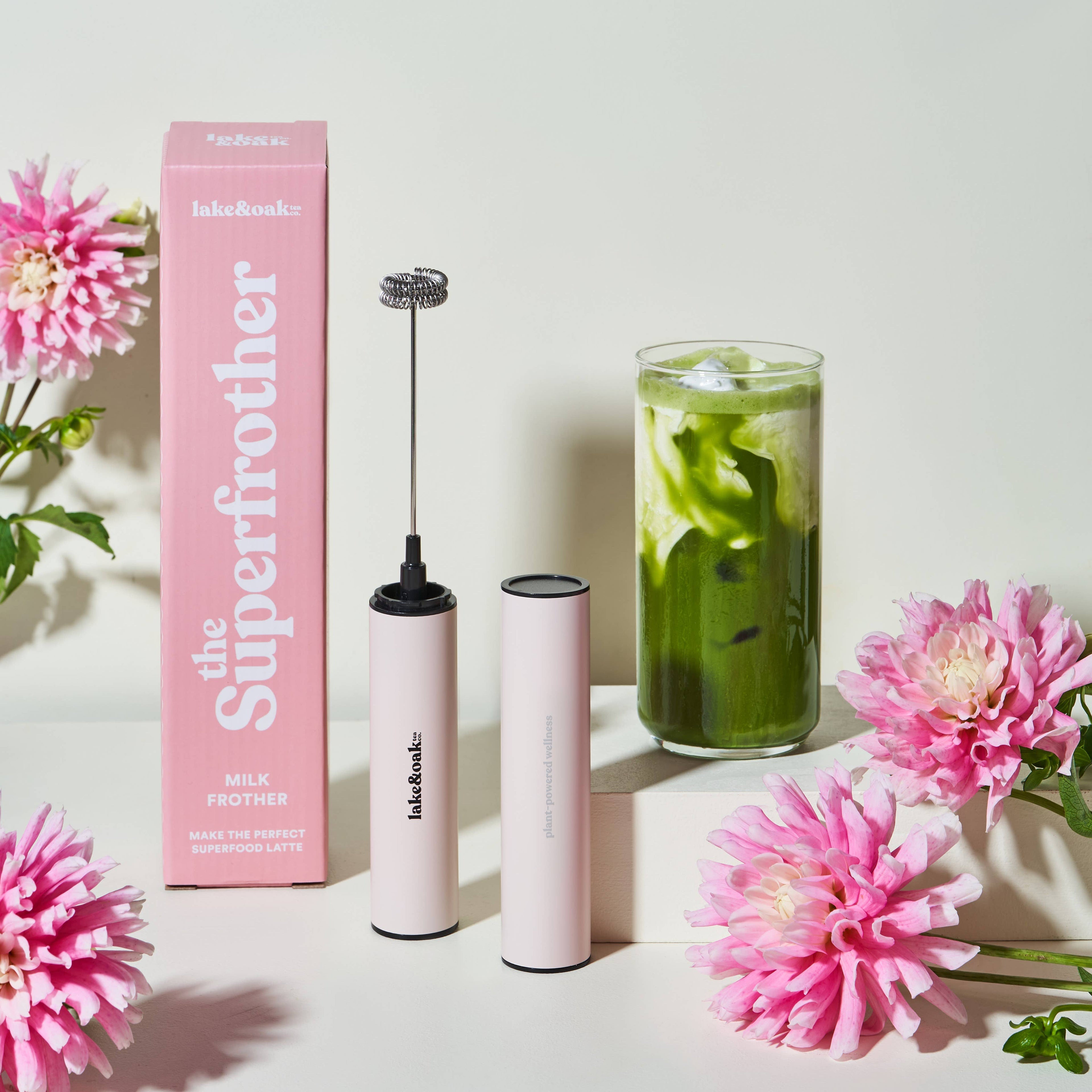 Pink milk frother with packaging and flowers on a light background