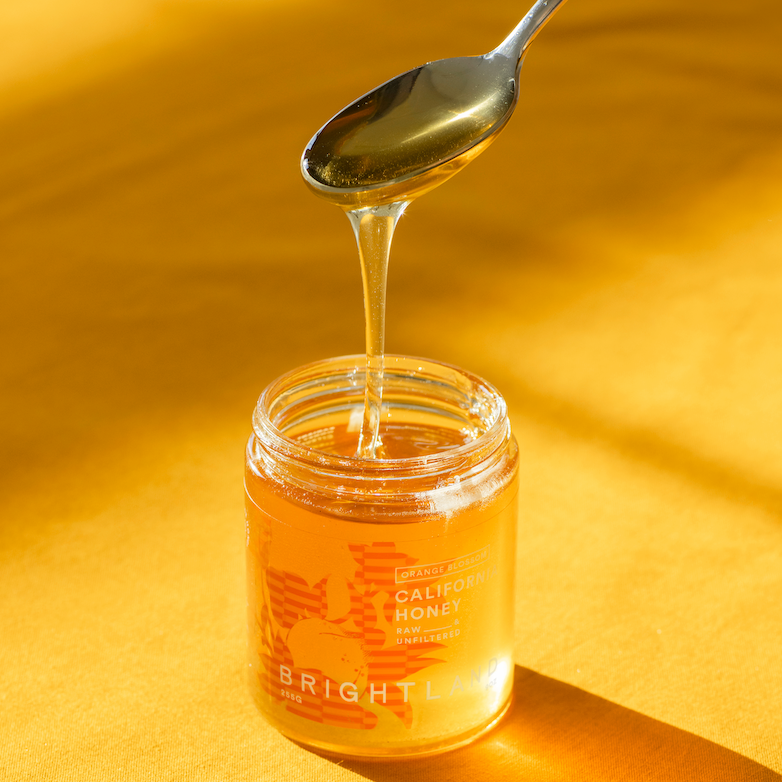 Jar of honey with a spoon dripping honey on a yellow background