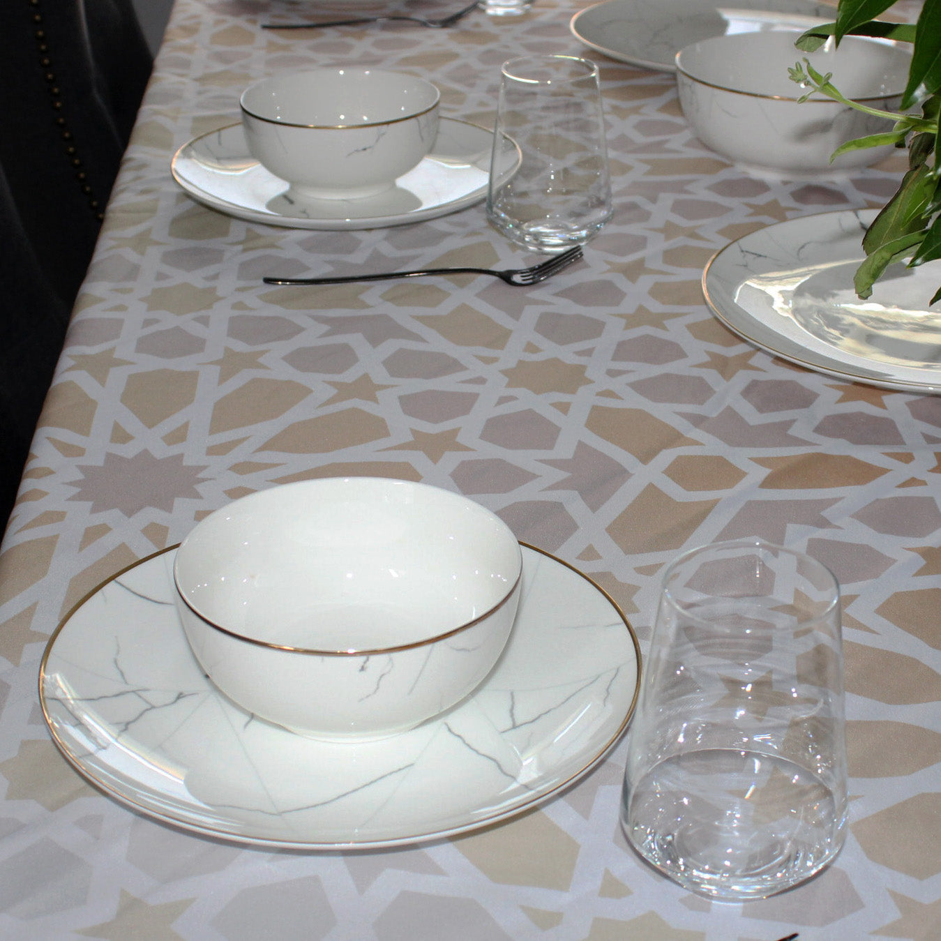 Dining table setting with white ceramic bowls and plates on a patterned tablecloth.
