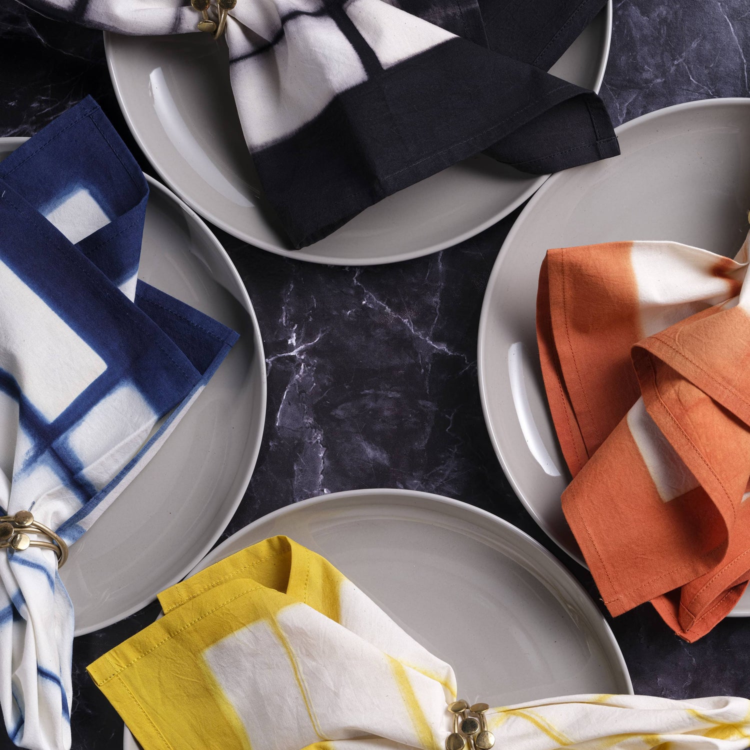 Plates with folded napkins in various colors on a dark marble surface
