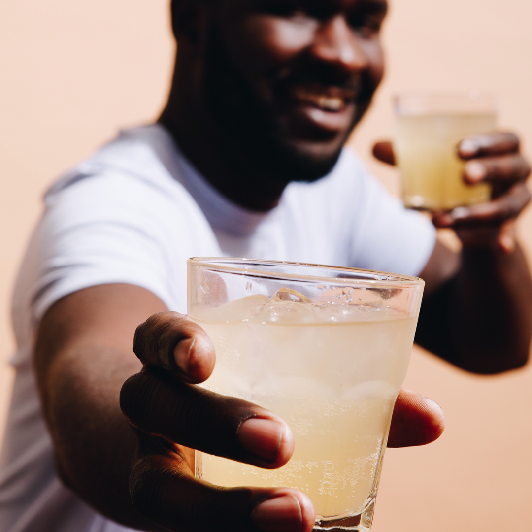 Two people holding glasses of a light-colored beverage against a neutral background