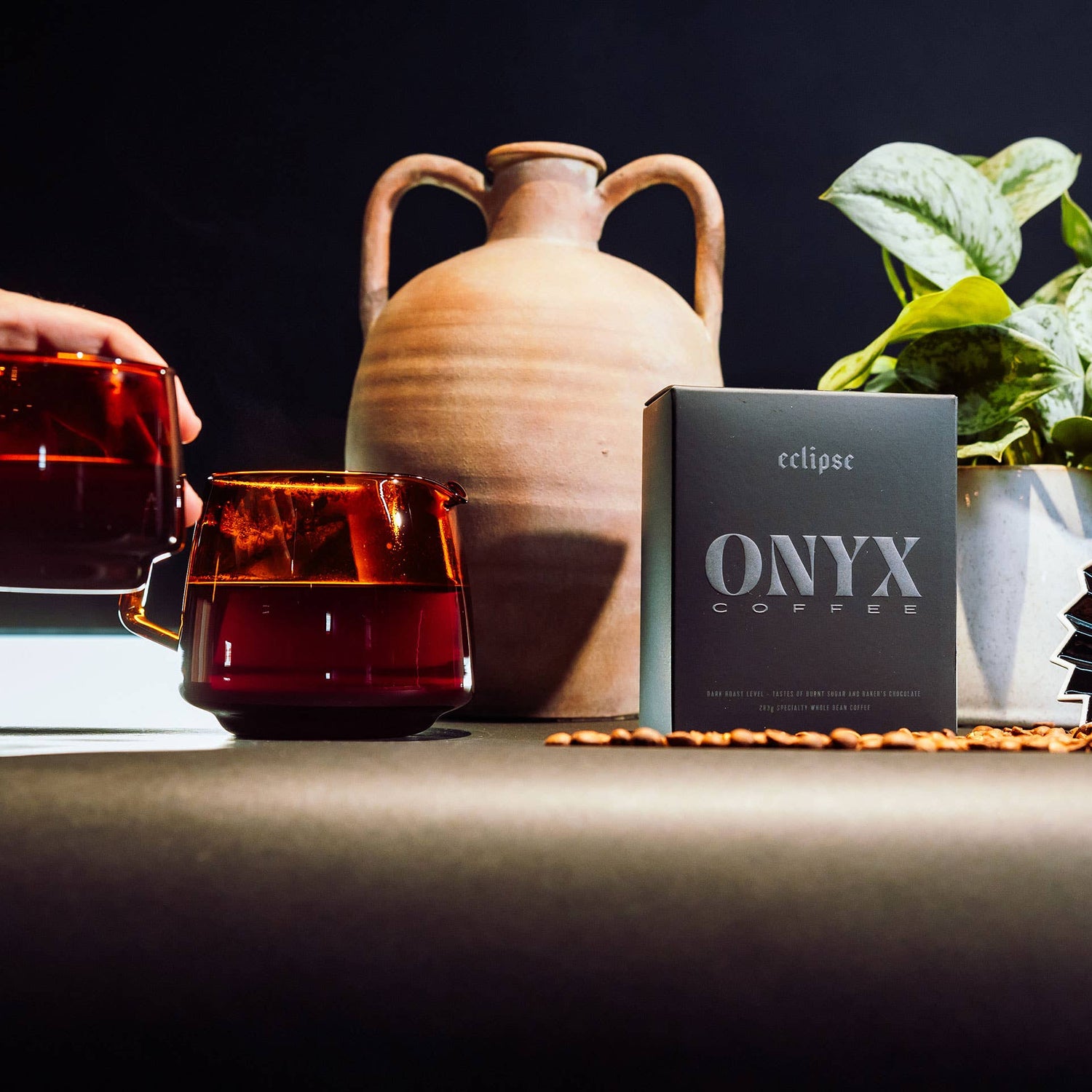 Onyx Coffee bag with coffee cups, a vase, and a plant on a dark background