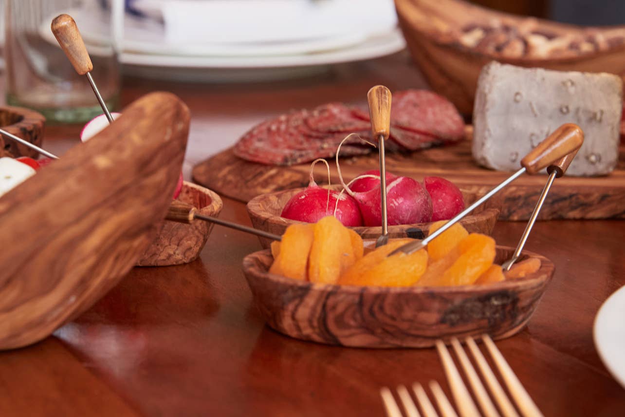 Italian Olivewood Aperitivo Bowls filled with radishes and dried fruit, with a meat and cheese platter in the background