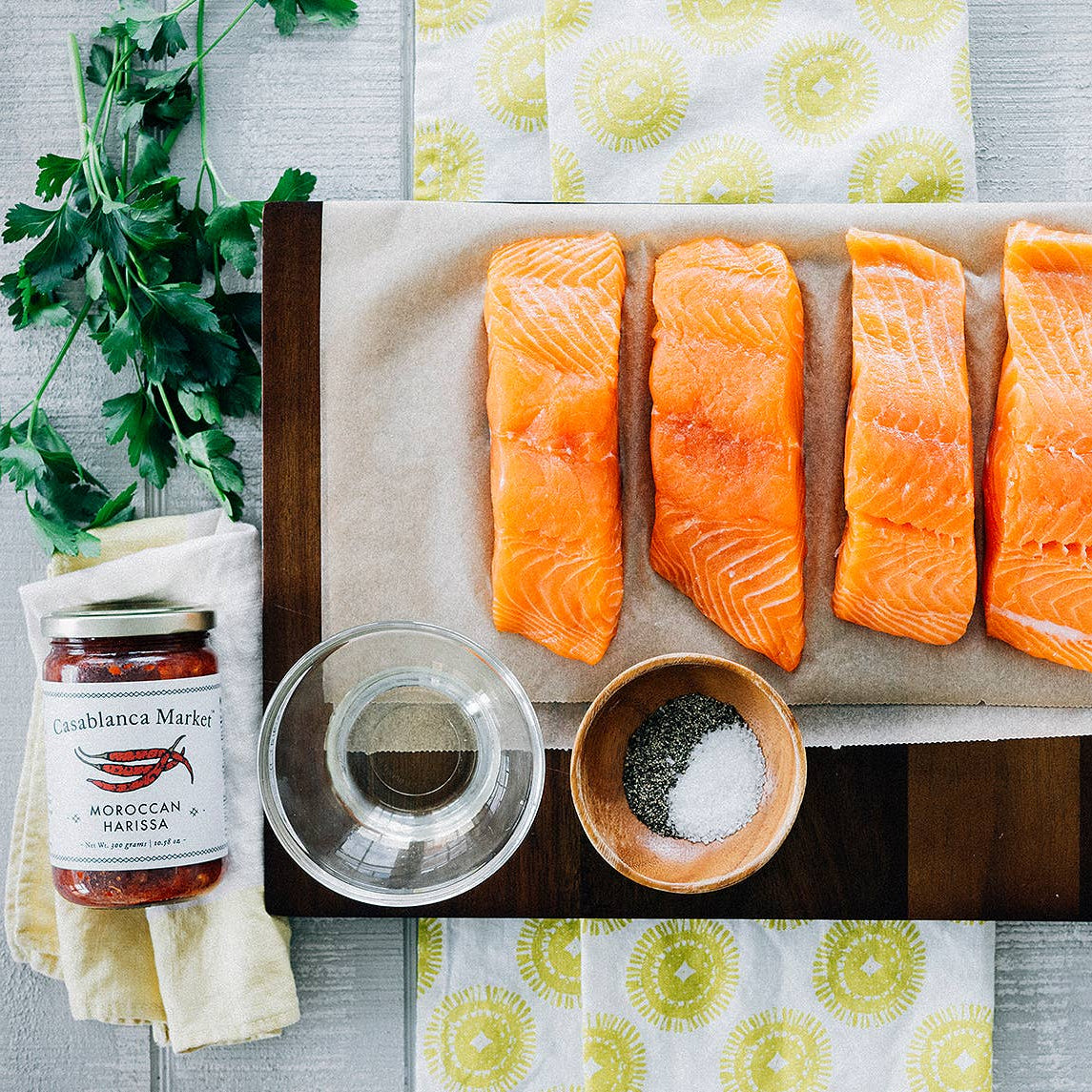 Raw salmon fillets on a cutting board with seasonings and sauces on a table.