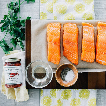 Raw salmon fillets on a cutting board with seasonings and sauces on a table.