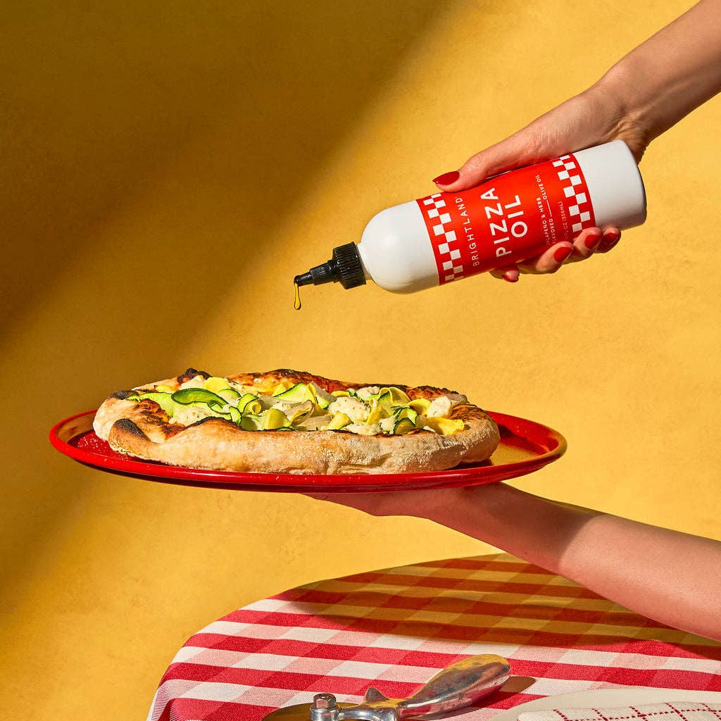 Person drizzling pizza oil over a pizza on a yellow background
