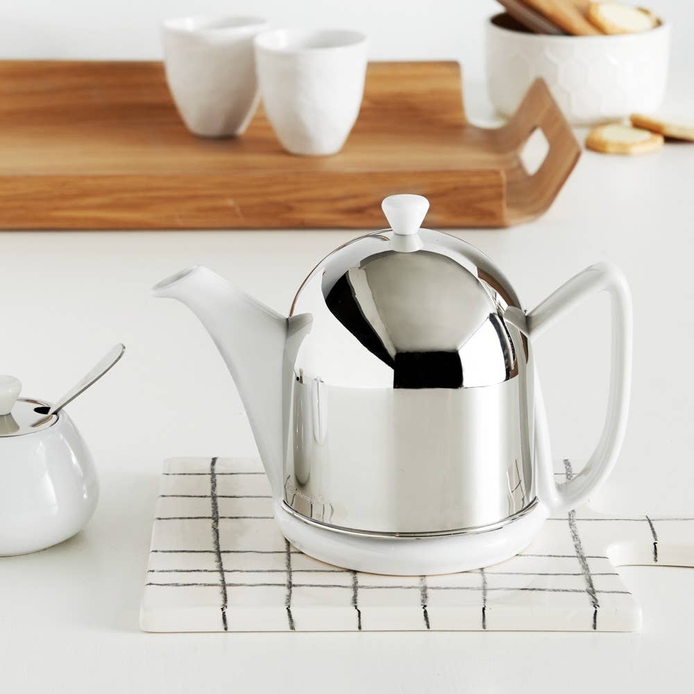 Silver teapot on a white surface with a wooden tray in the background