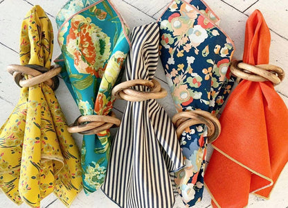 Set of colorful napkins tied with wooden bangle napkin rings on a light wooden surface
