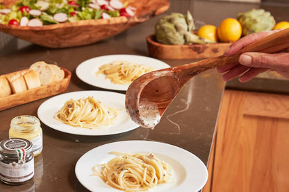 Pasta sauce being poured over a dish of pasta from an Italian Olivewood Soup and Pasta Ladle