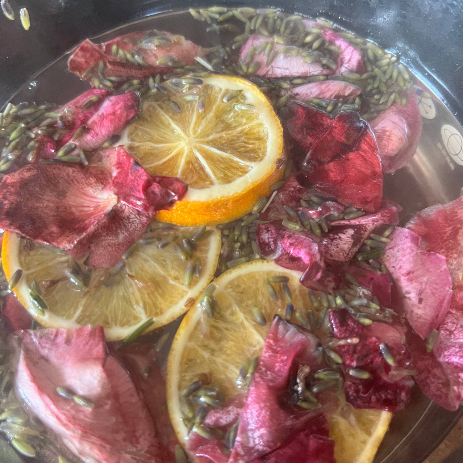 Infused water with lemon slices, pink flowers, and herbs in a glass bowl.