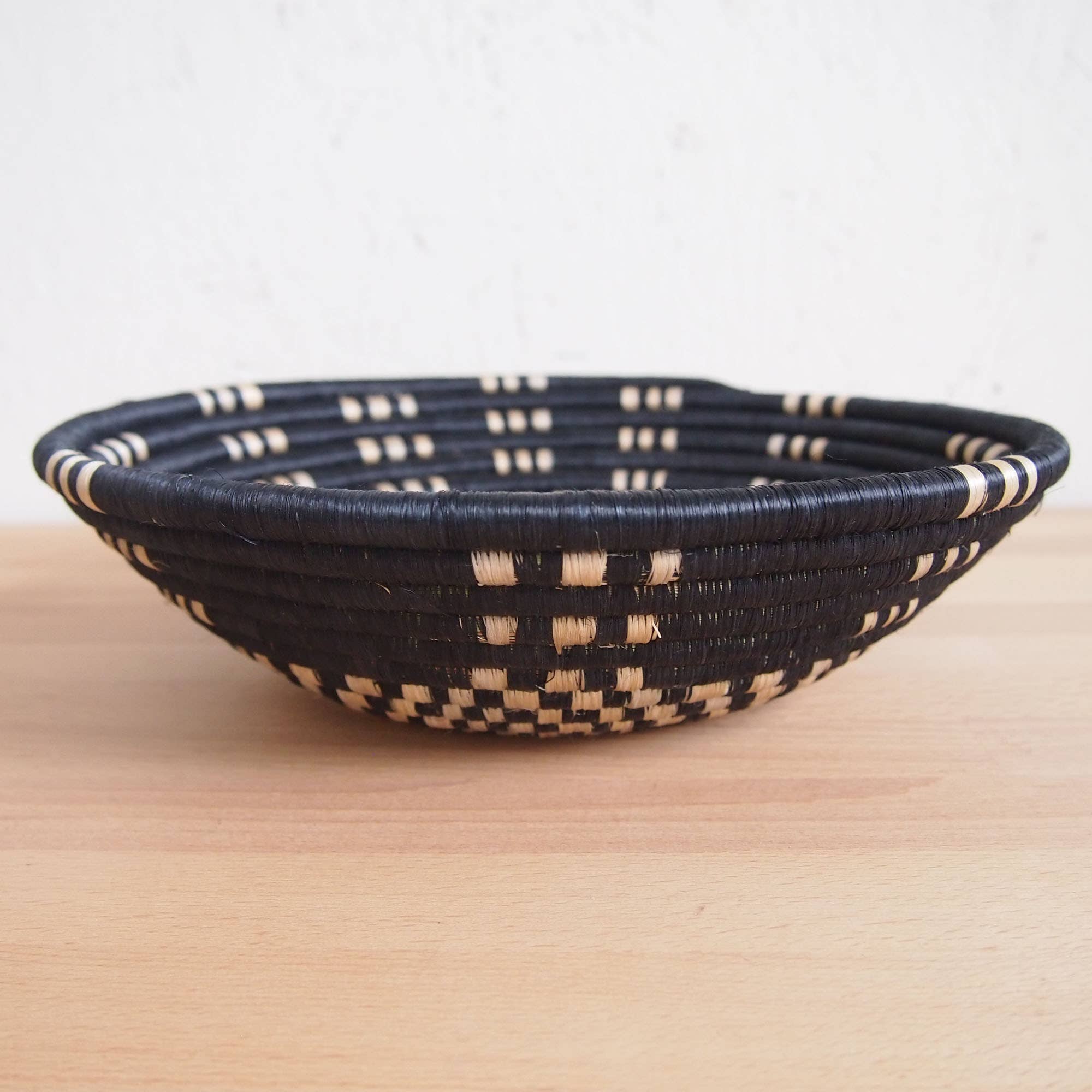 Woven black and beige bowl on a light wooden surface with a white background