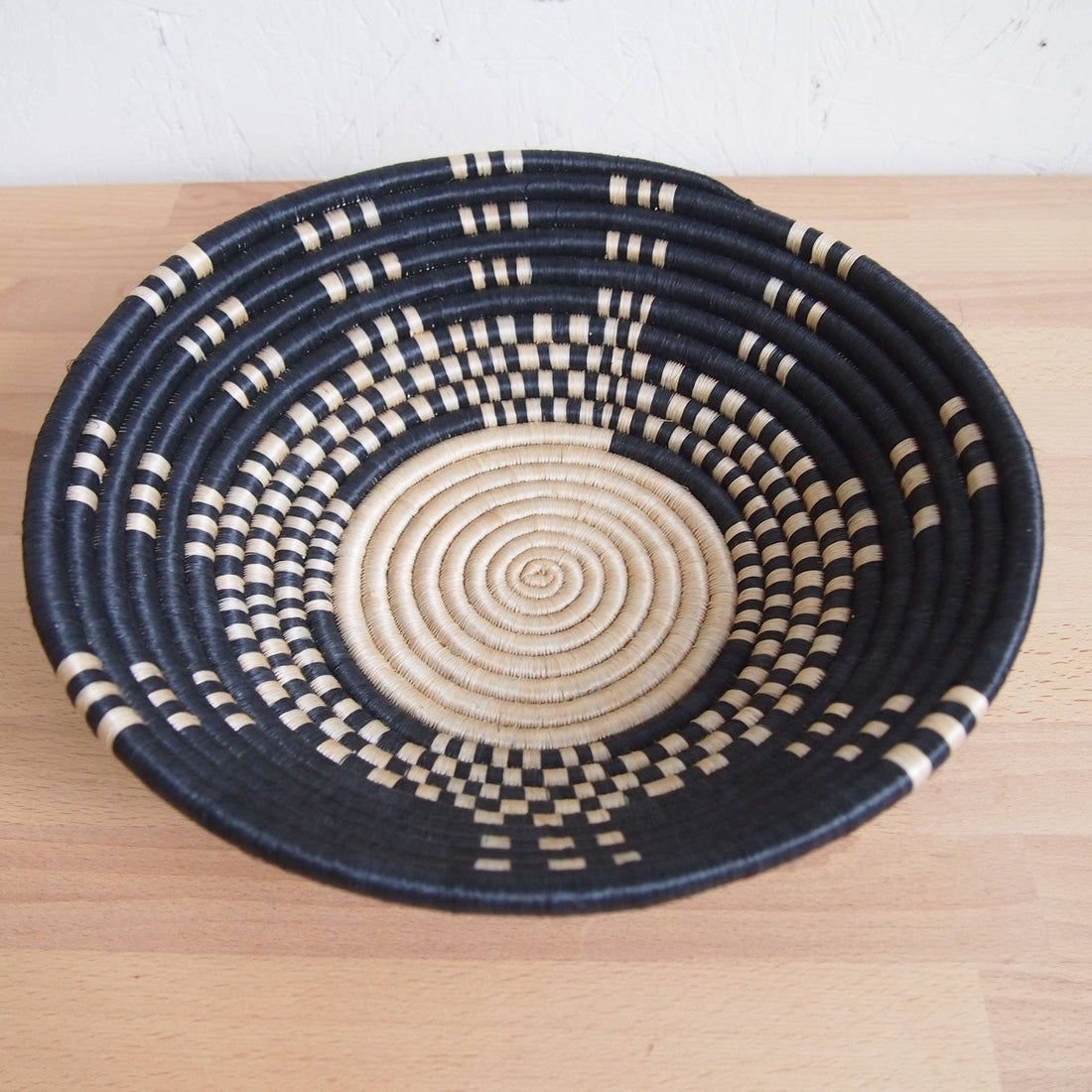 Woven basket with black and beige pattern on a wooden surface