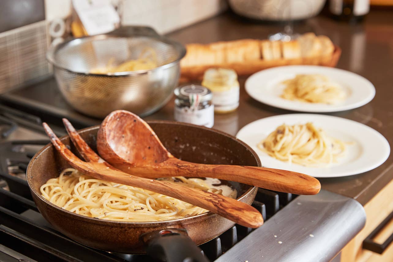 A pan of pasta with an Italian Olivewood Soup and Pasta Ladle and serving fork over the top