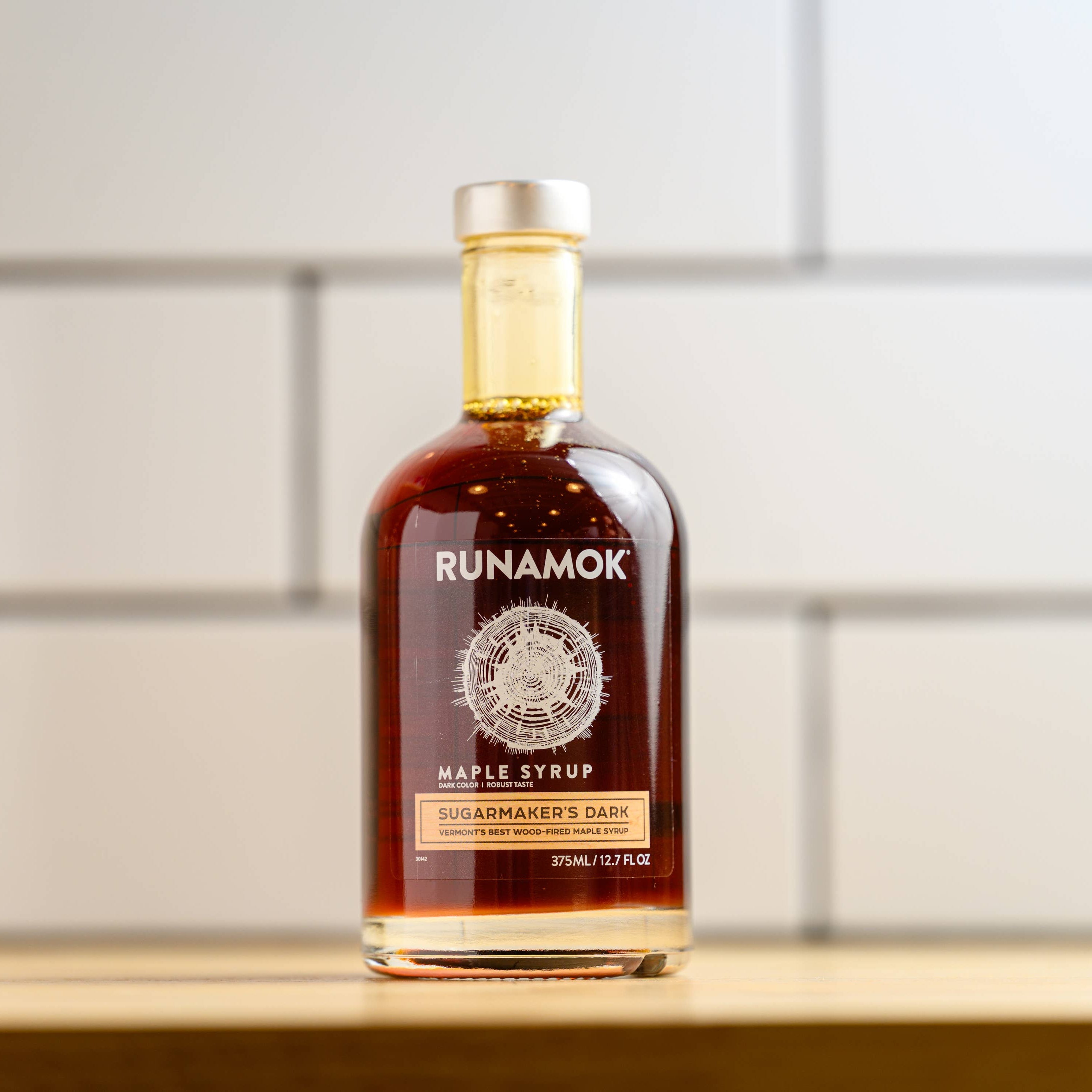 Bottle of Runamok maple syrup on a wooden surface with a tiled wall background
