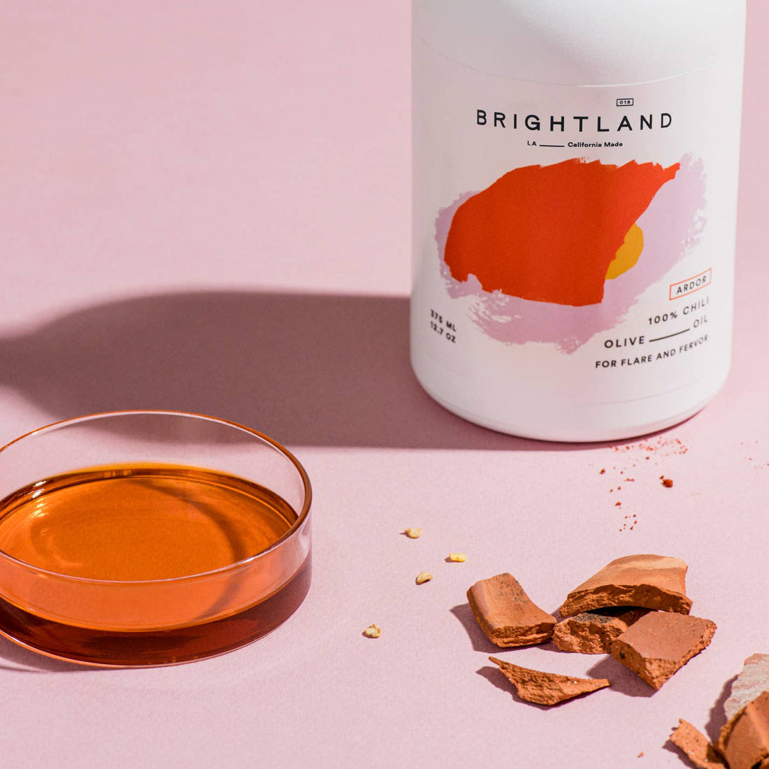 Bottle of Brightland olive oil with a bowl of oil and crackers on a pink background