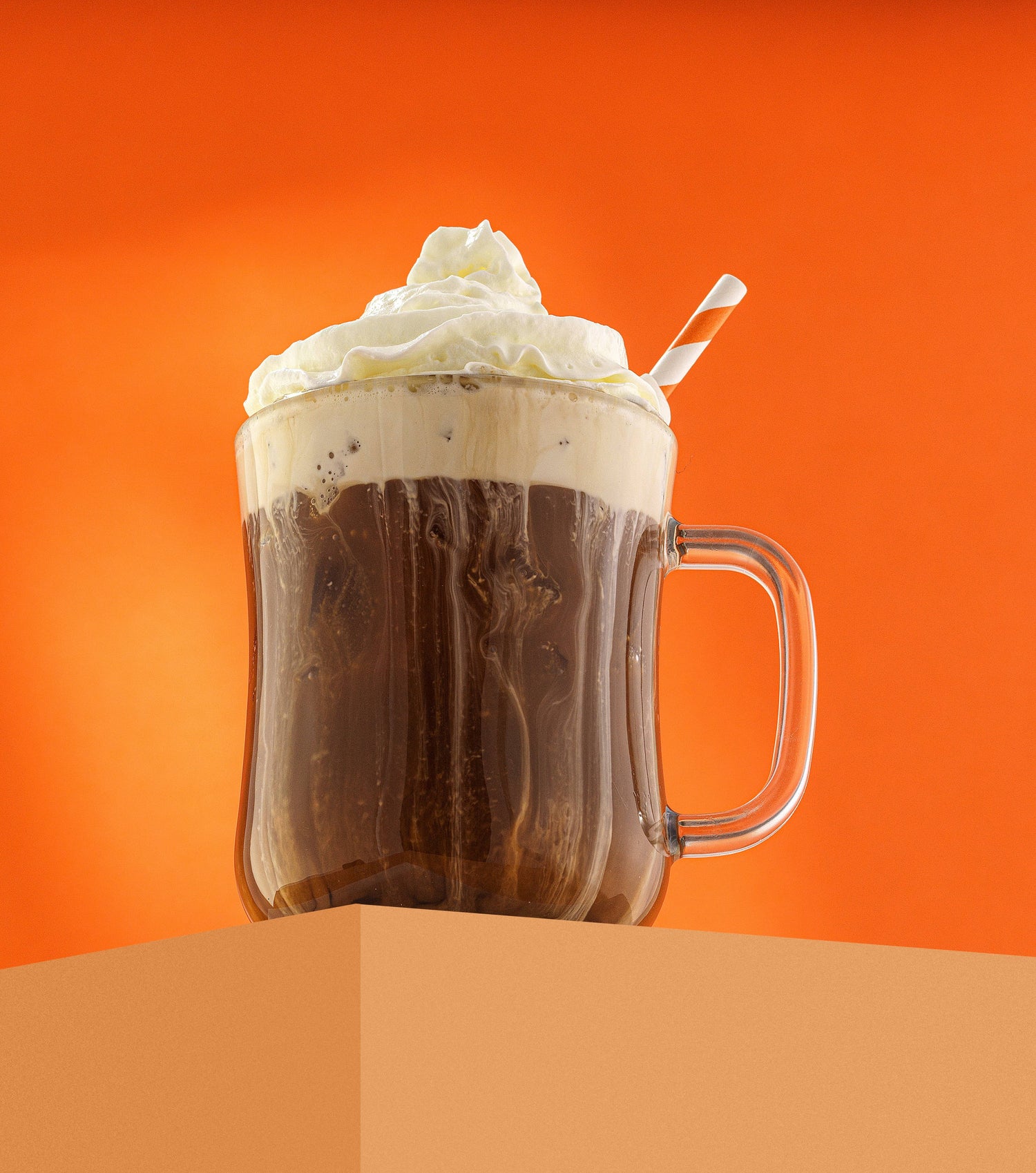Glass mug filled with a creamy hot chocolate drink against an orange background