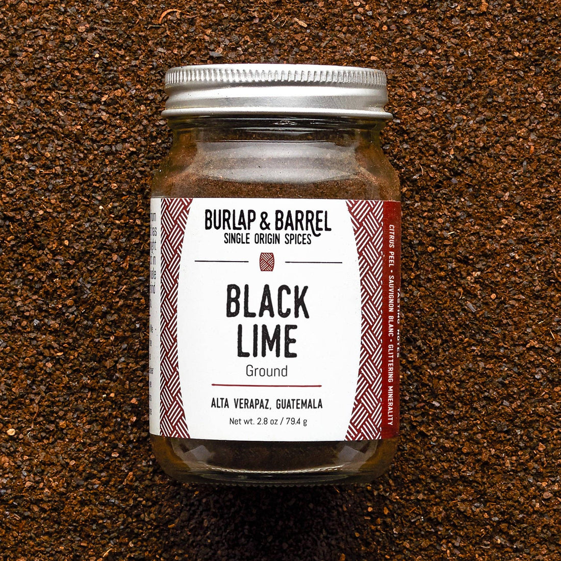 Jar of Black Lime ground spice from Burlap &amp; Barrel on a textured brown background